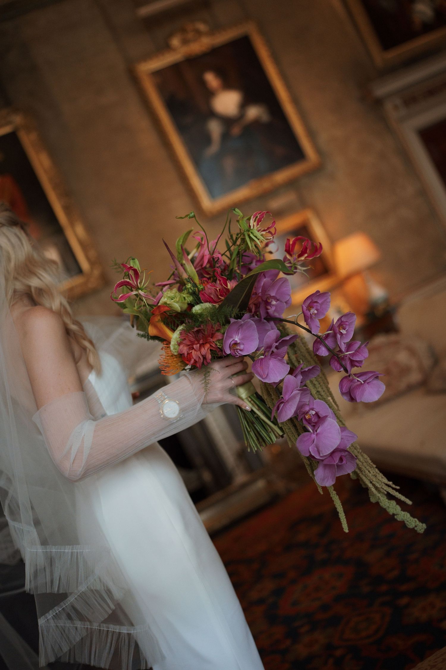 Wedding bouquet with purple orchids and greenery held against a white dress in an elegant indoor setting.