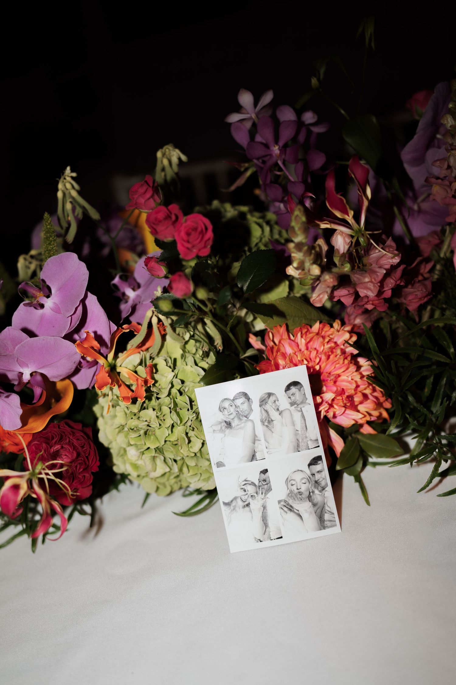 Floral arrangement with colorful flowers and photographs displayed on white surface.