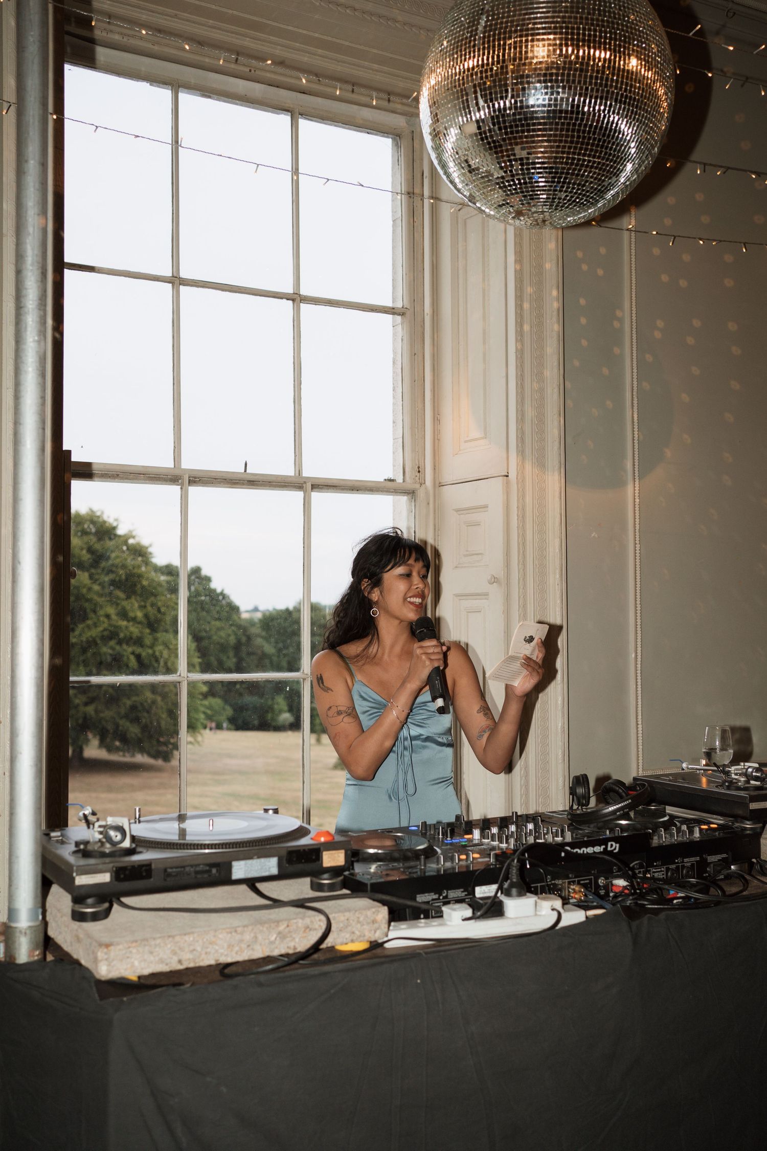 DJ equipment setup with disco ball and large windows in elegant white room.