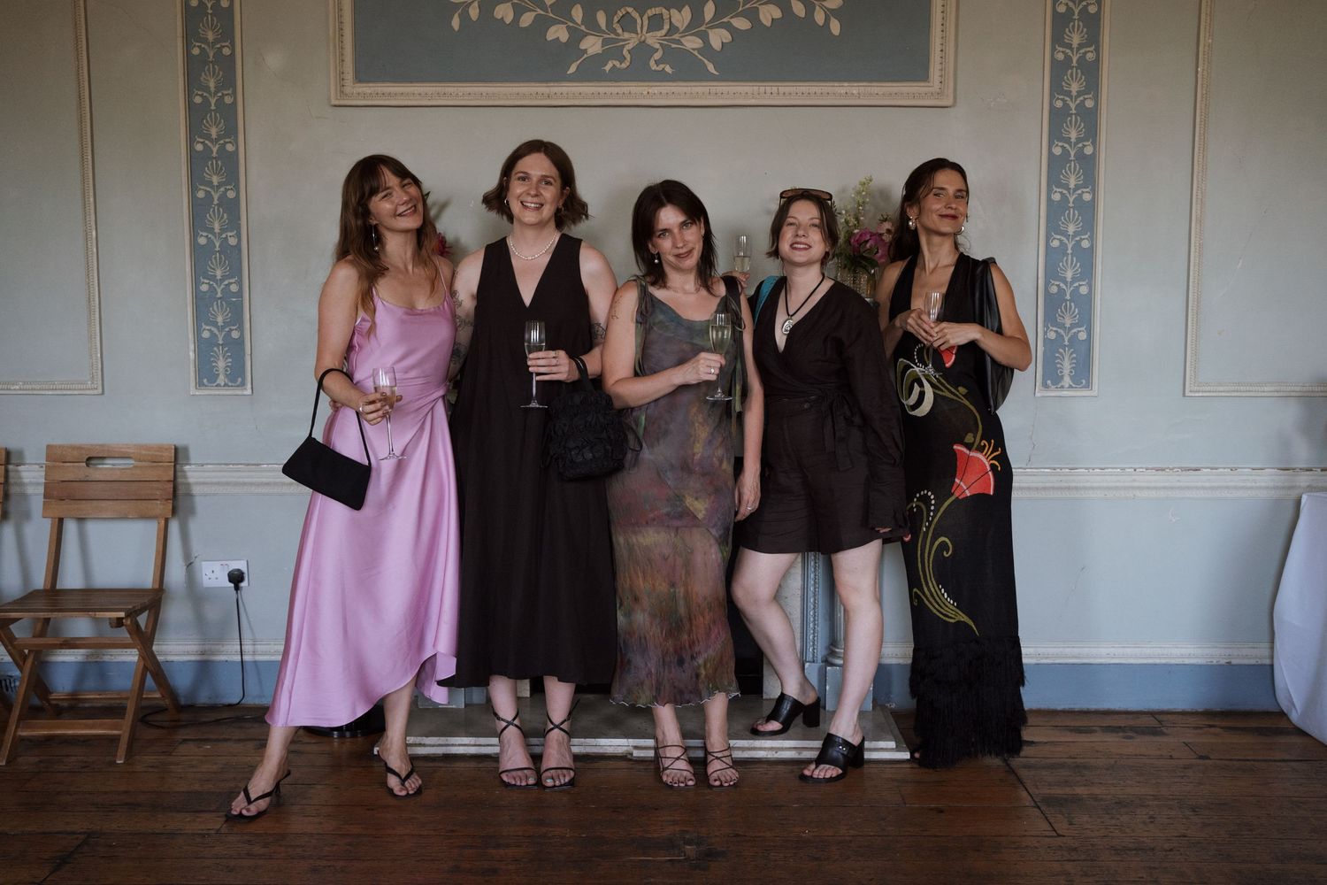 Group of party guests in formal attire gathered in an elegant room with patterned wallpaper.