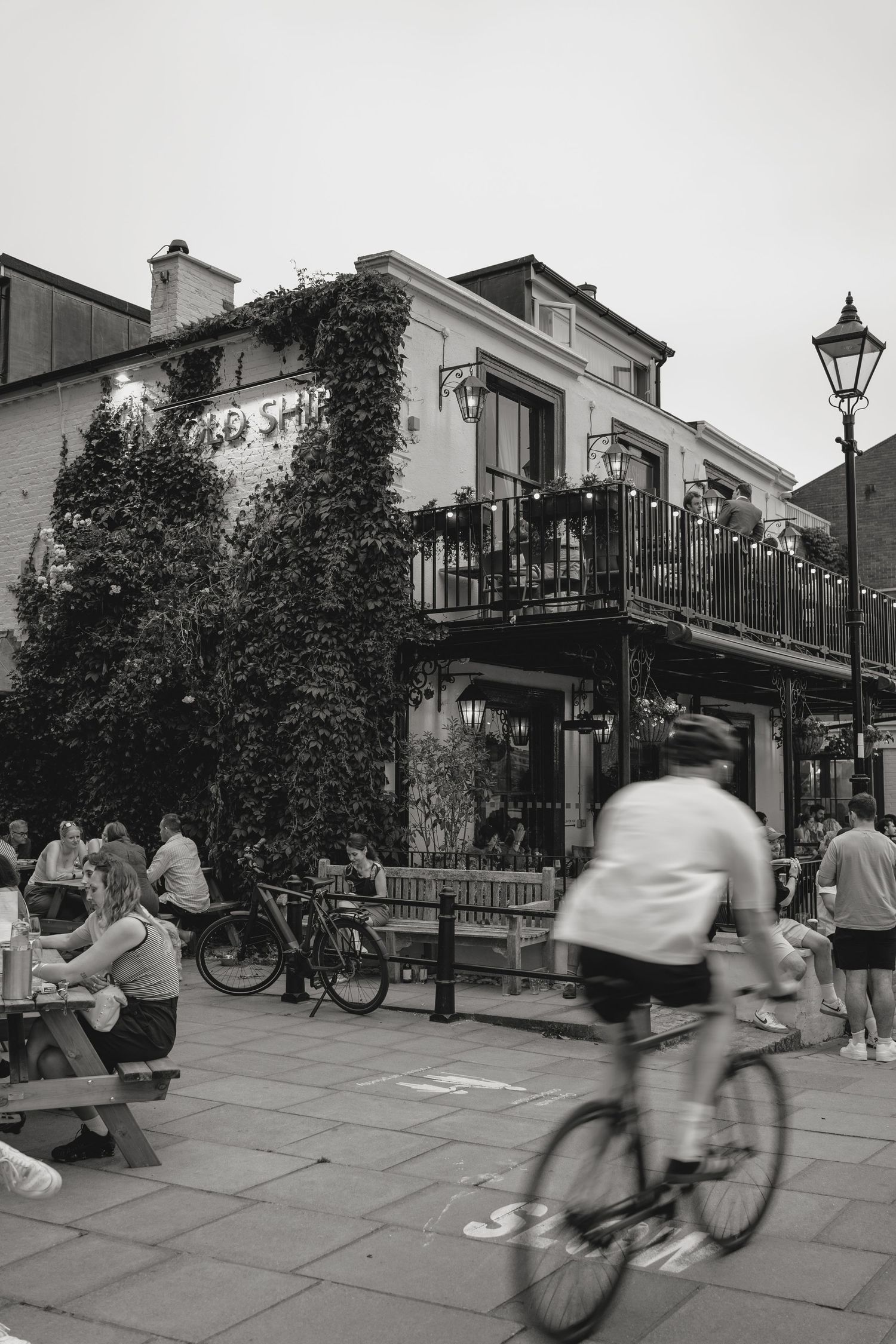 Black and white street scene with cyclists and pedestrians passing by historic buildings with balconies.