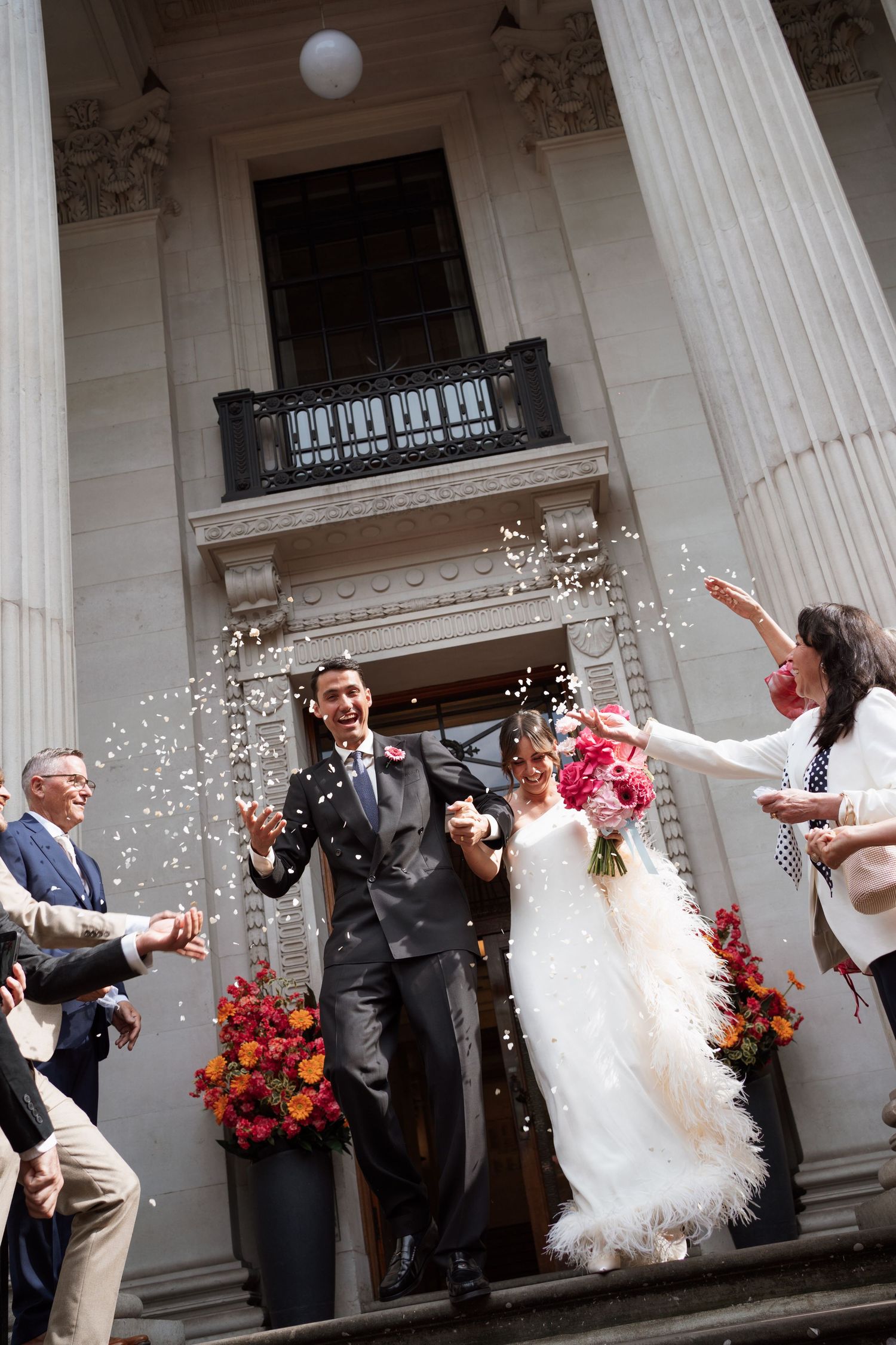 Celebration outside columned building with confetti and bright flowers.