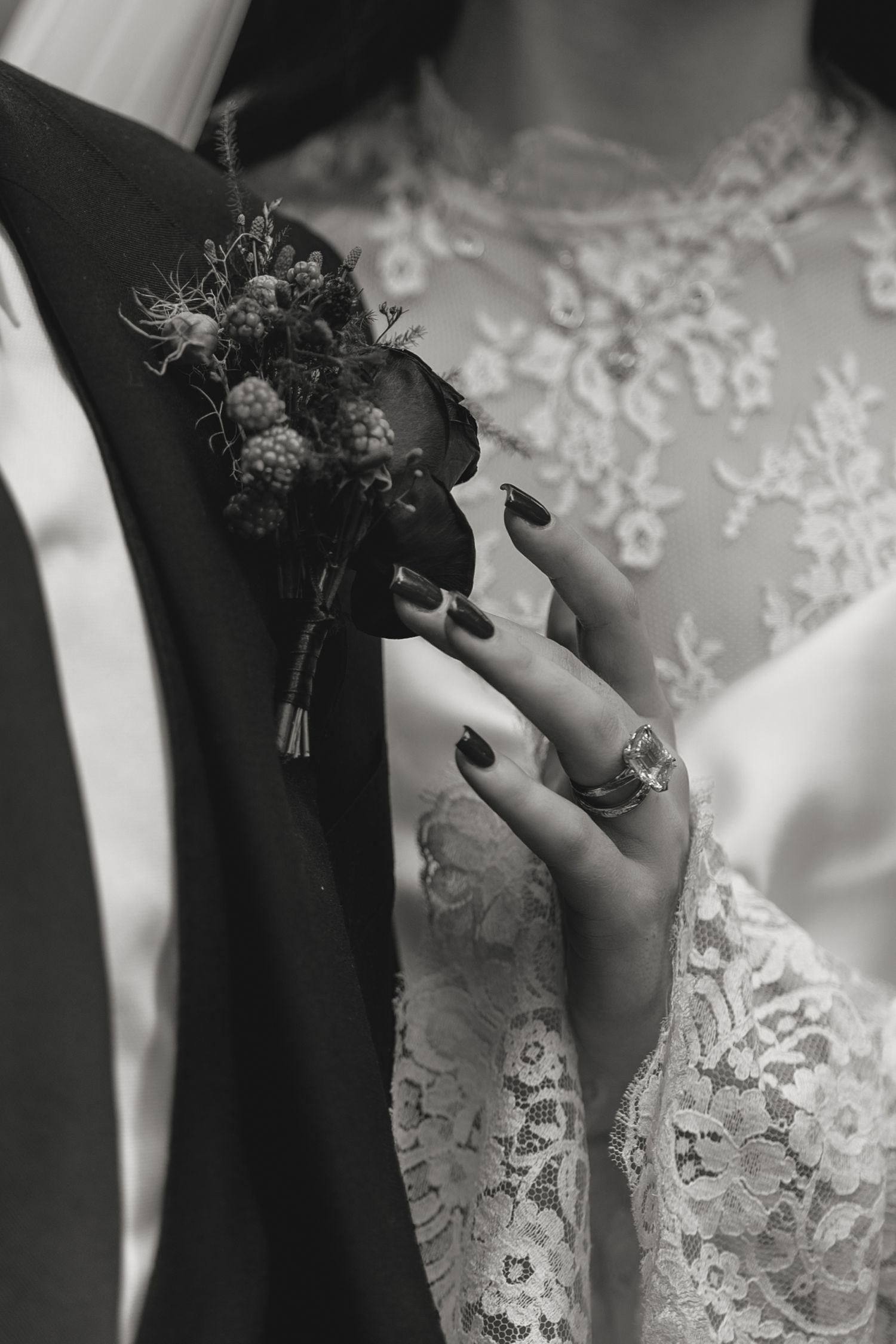 Close-up of a boutonniere and lace detail on wedding attire with delicate hand placement.
