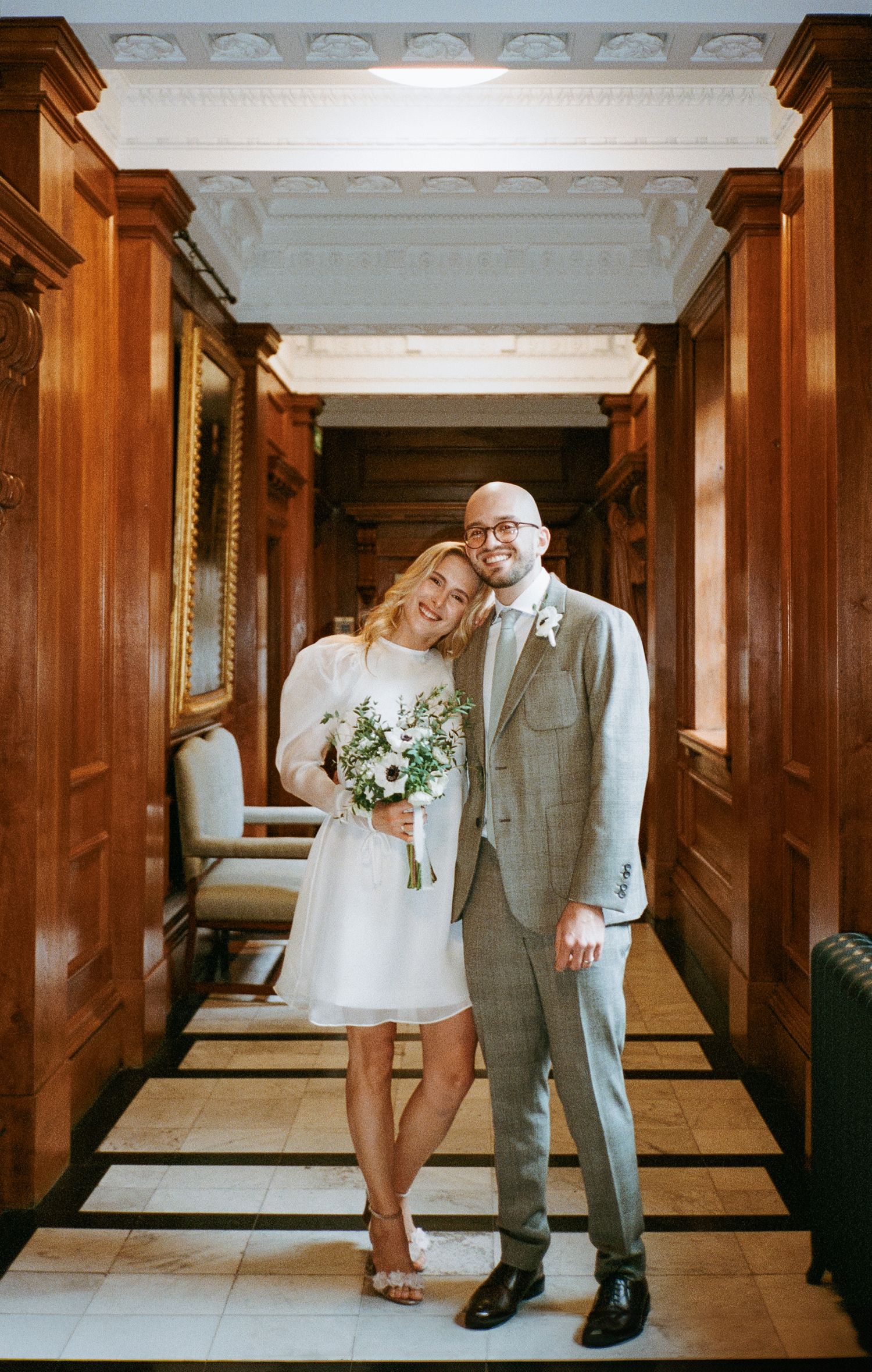 Wedding couple posing playfully in an elegant wood-paneled hallway.