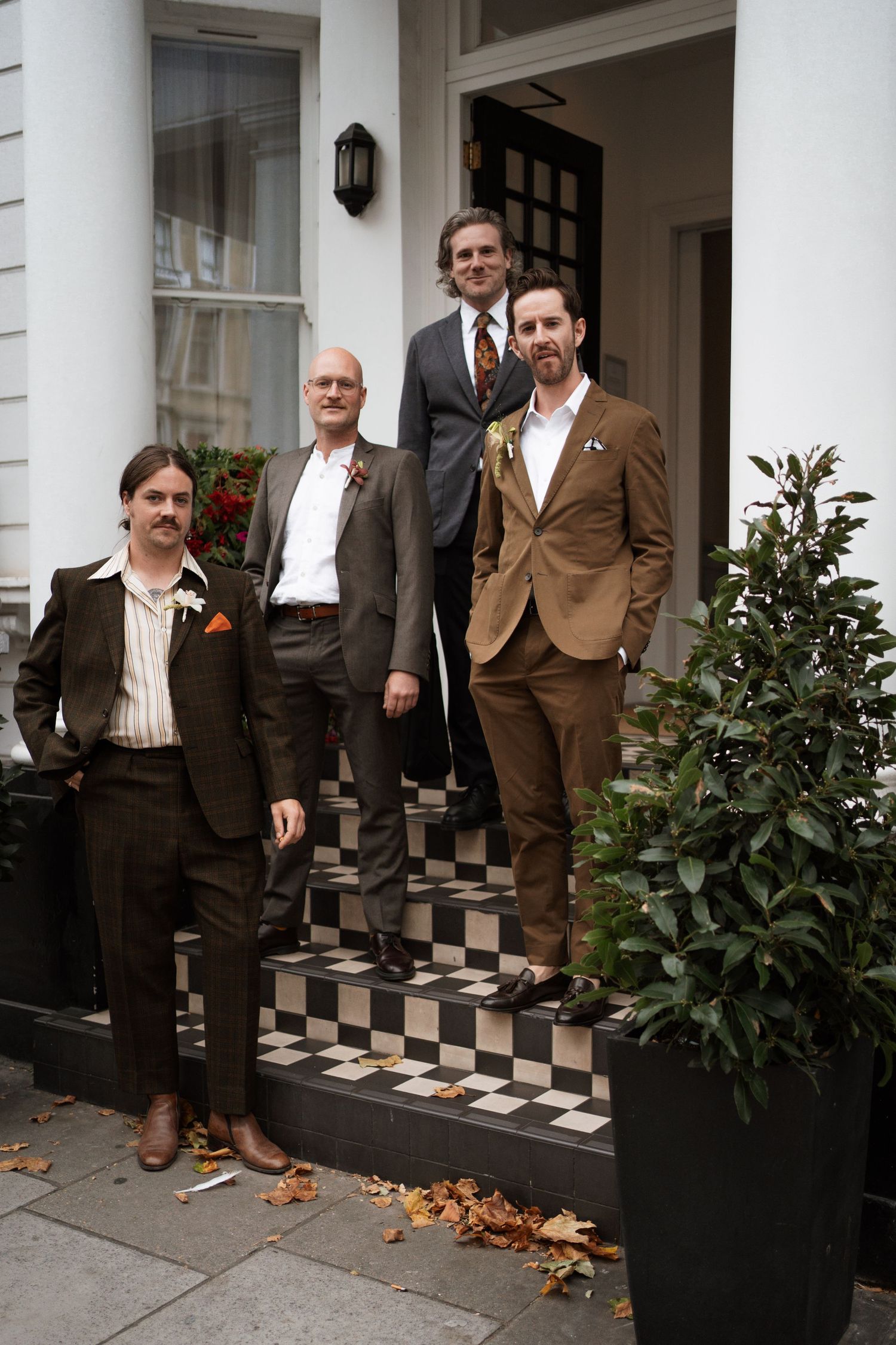 Group in brown suits standing on black and white checkered porch steps.