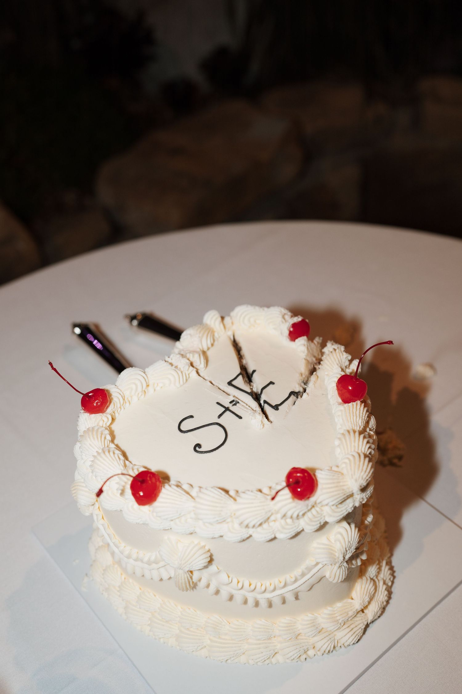 Close-up of an elegant white wedding cake with cherry decorations and monogram details.