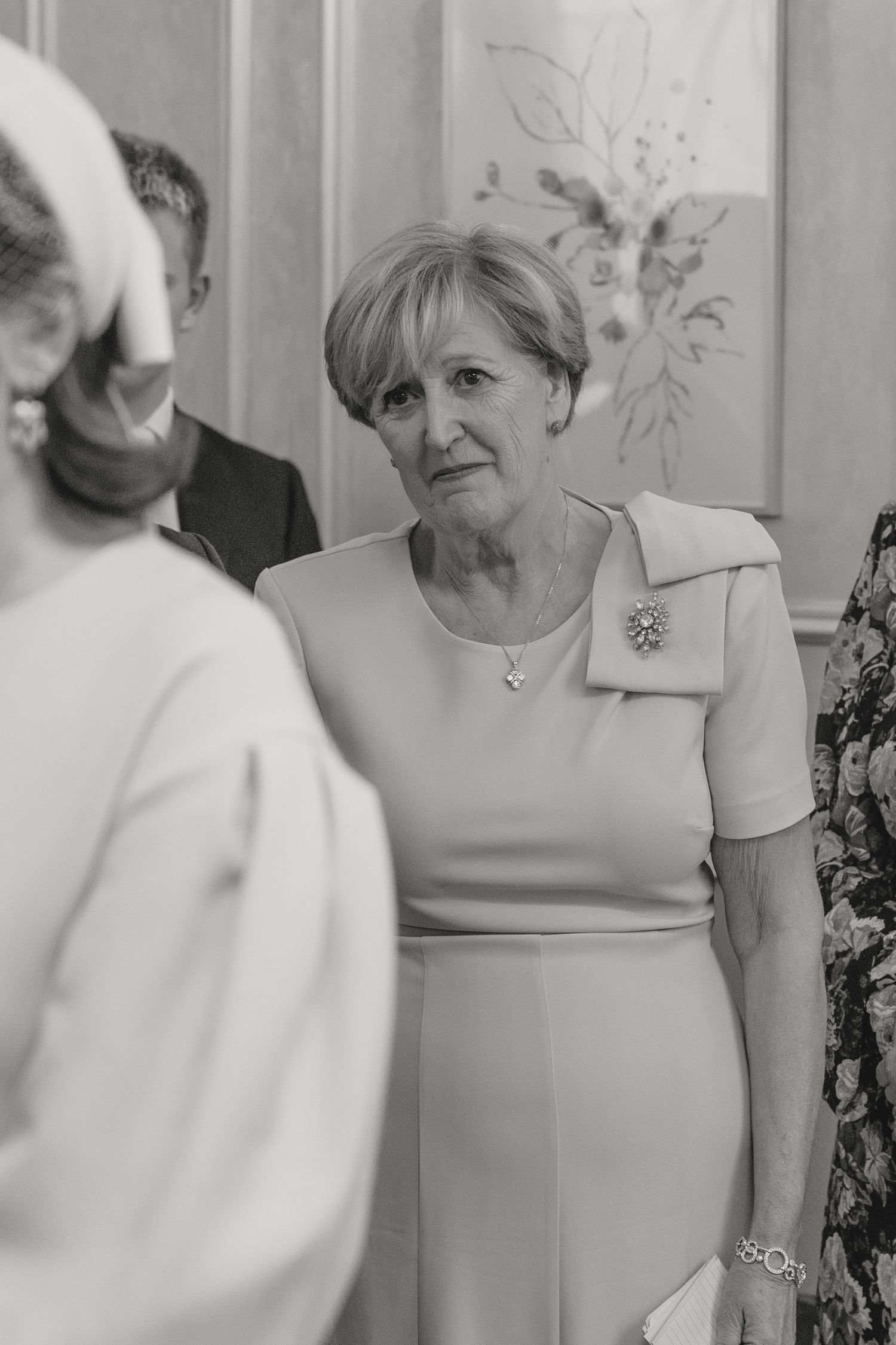 A woman in a light-colored dress with a brooch at a formal gathering.