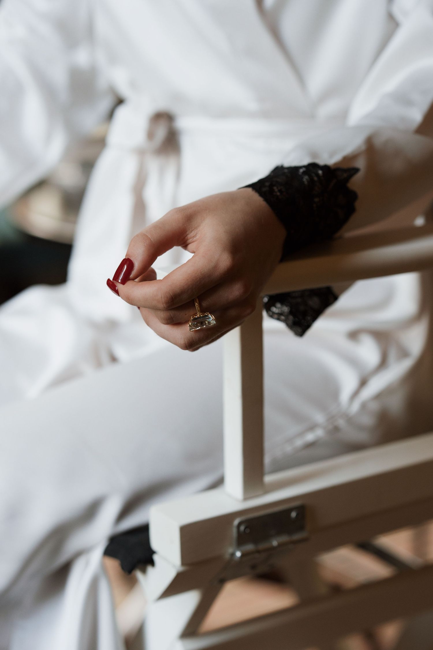 Close-up of hands with red nails and black lace sleeves against white fabric.