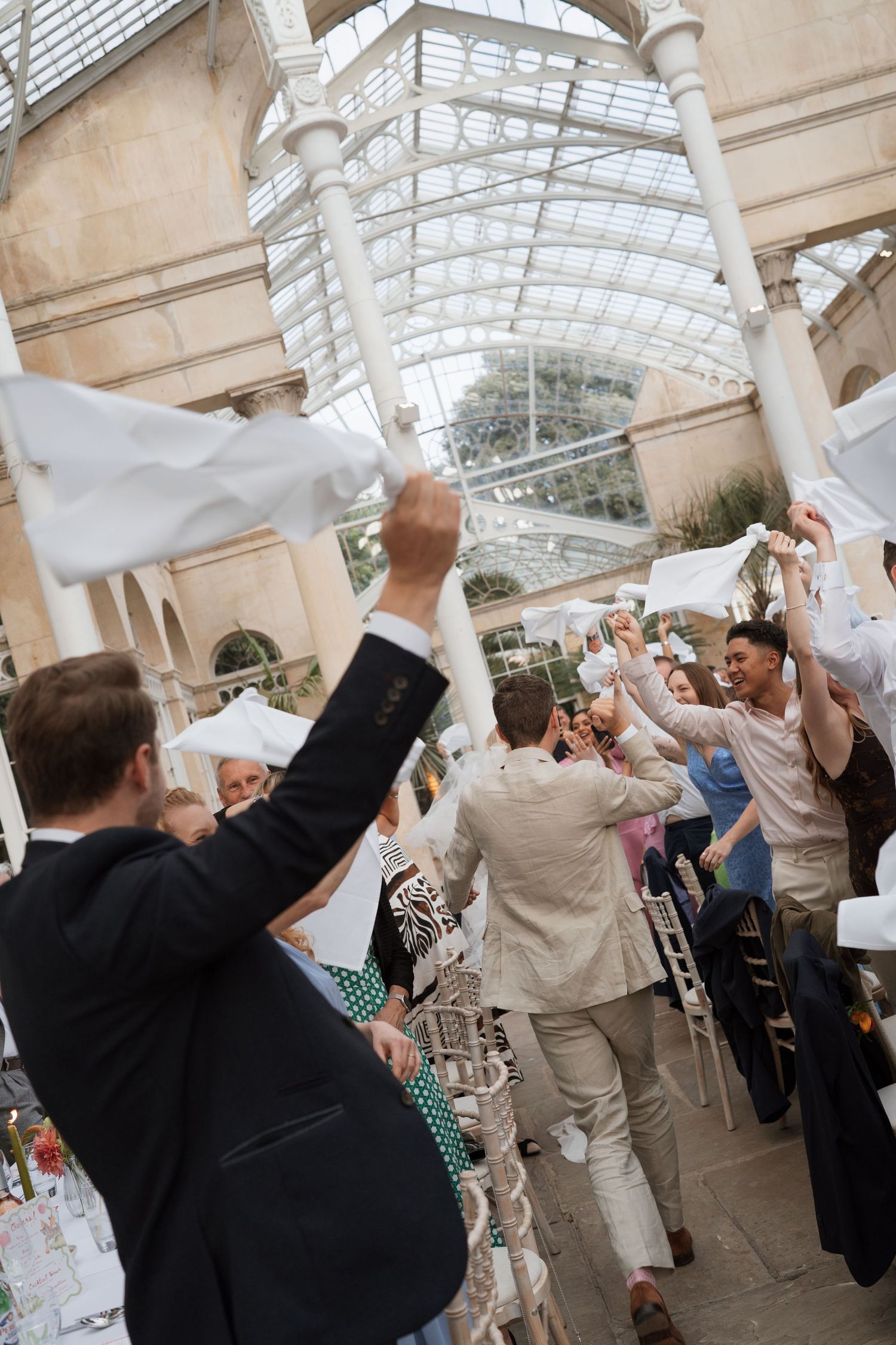 Celebration scene with guests waving white napkins in a bright conservatory setting.