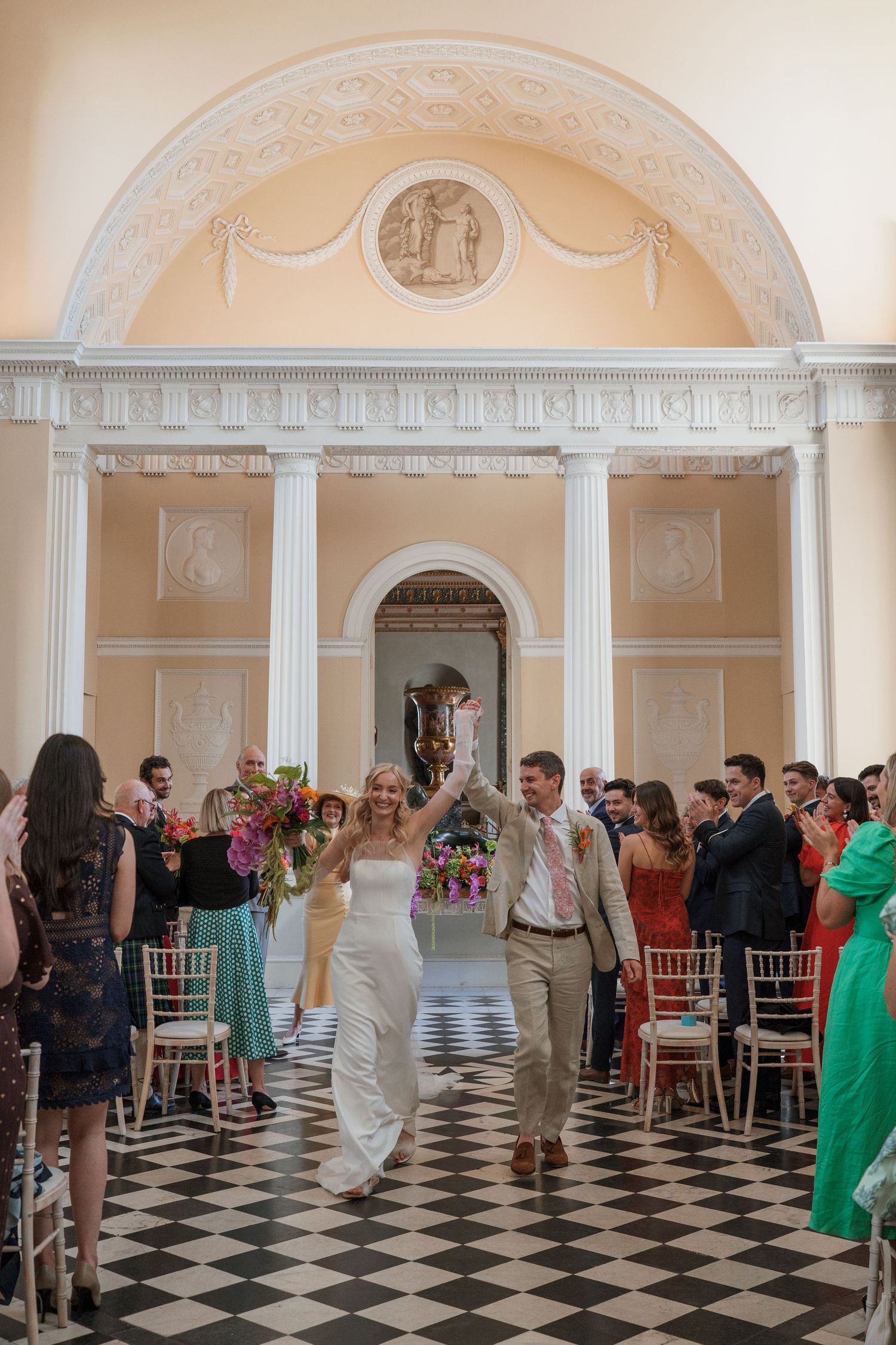 Guests mingle in a grand hall with black and white checkered floors and ornate archways.