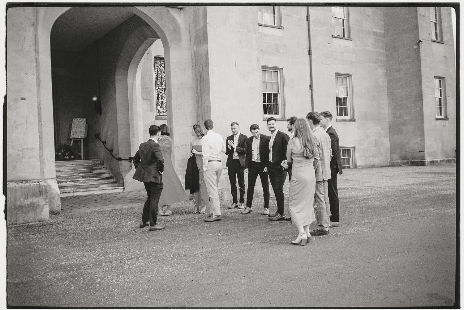 People walking along the exterior of a historic stone building.