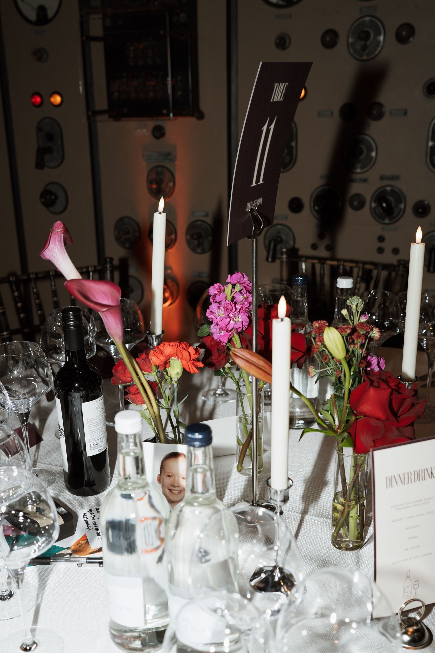Elegant table setting with white candles, wine glasses, and colorful floral arrangements.