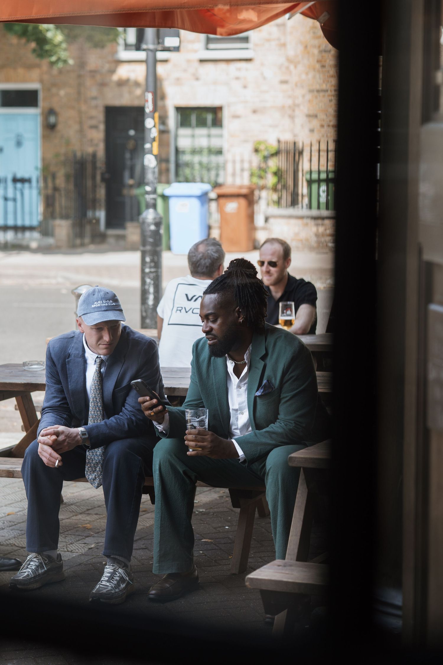 People sitting on outdoor benches checking their phones in an urban setting.