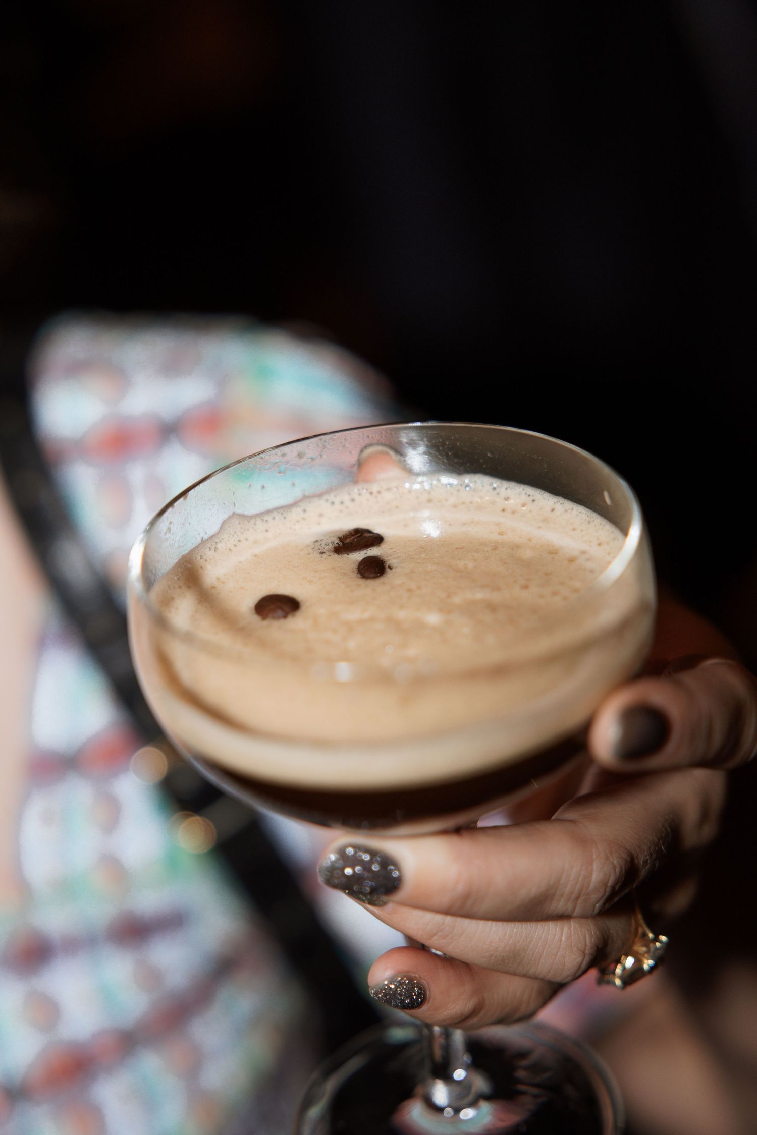 Hands holding a creamy cocktail garnished with coffee beans in a coupe glass.
