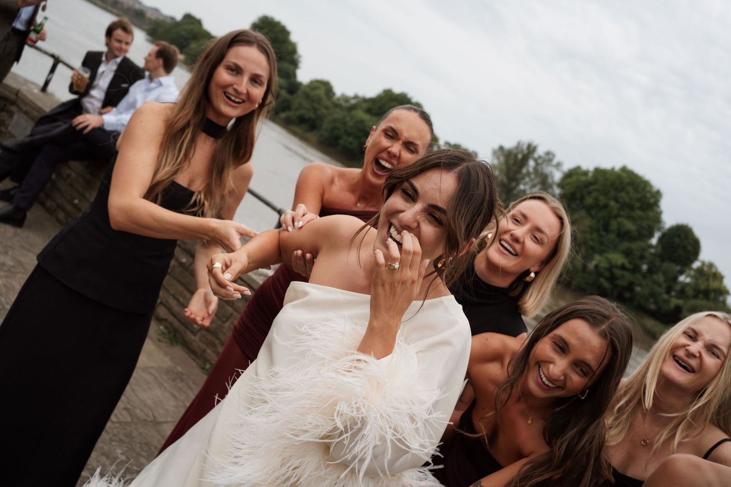 A group celebrates with feather boas and laughter during a wedding photoshoot.