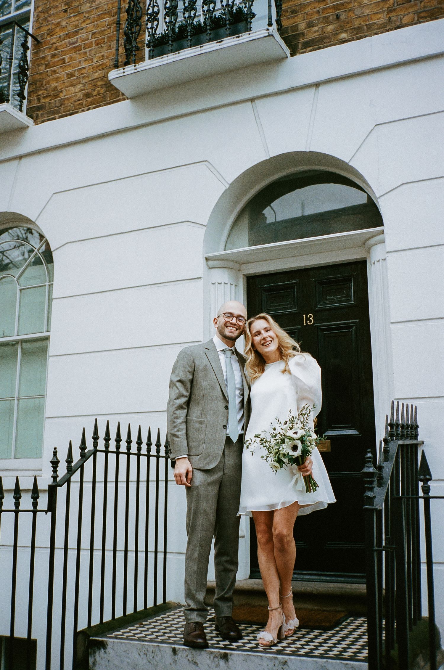 Newlyweds posing outside a classic London townhouse with white facade and iron railings.
