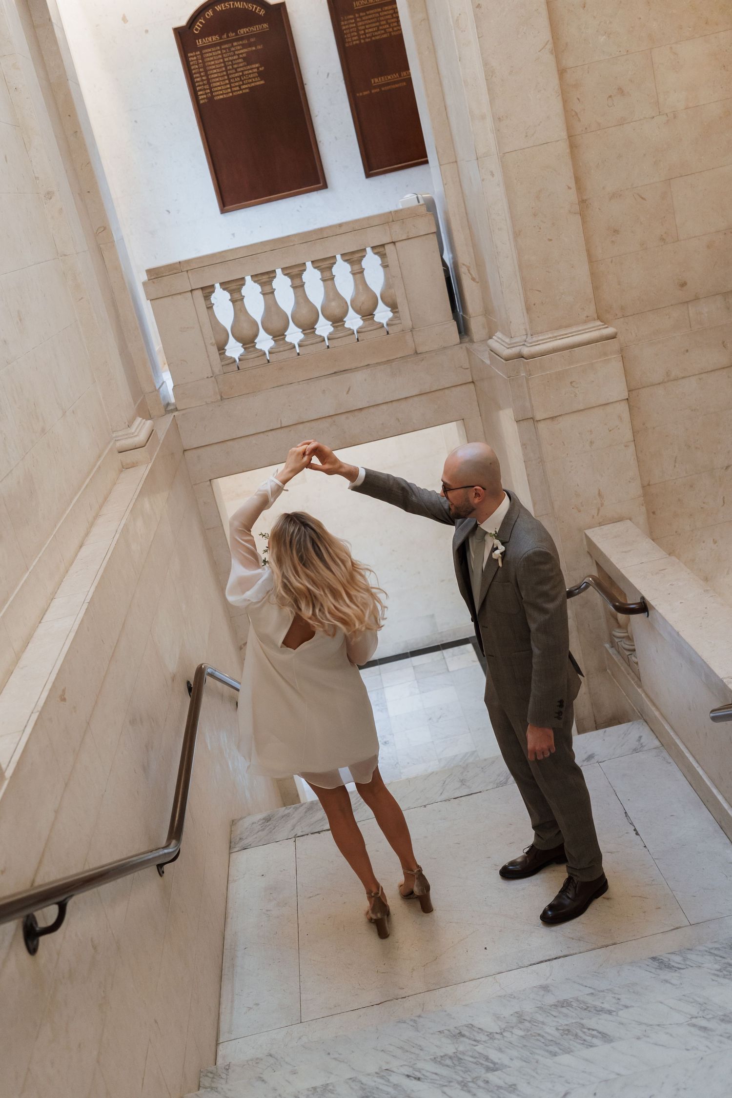 A couple dancing on elegant marble stairs inside a historic building with white balustrades.