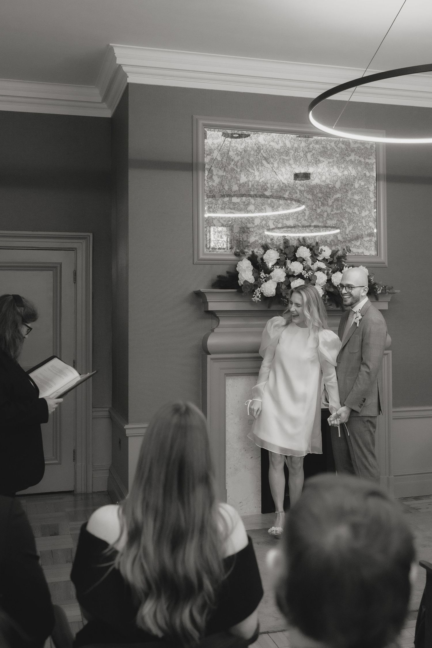 An intimate wedding ceremony in progress with guests seated in a grey-walled room.