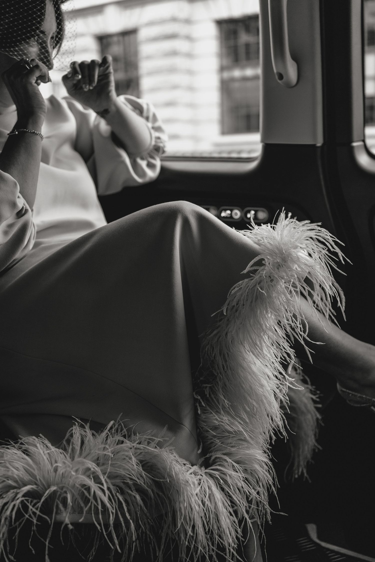 Black and white photo showing feather-trimmed dress details in a car interior.