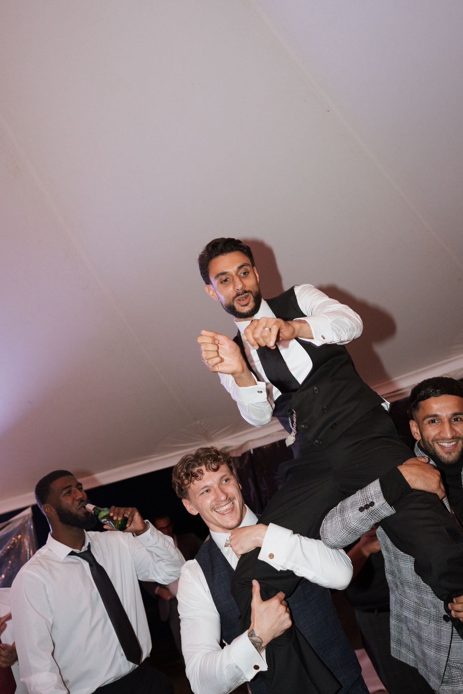 Groomsmen in formal black and white attire dancing and celebrating at a wedding reception.