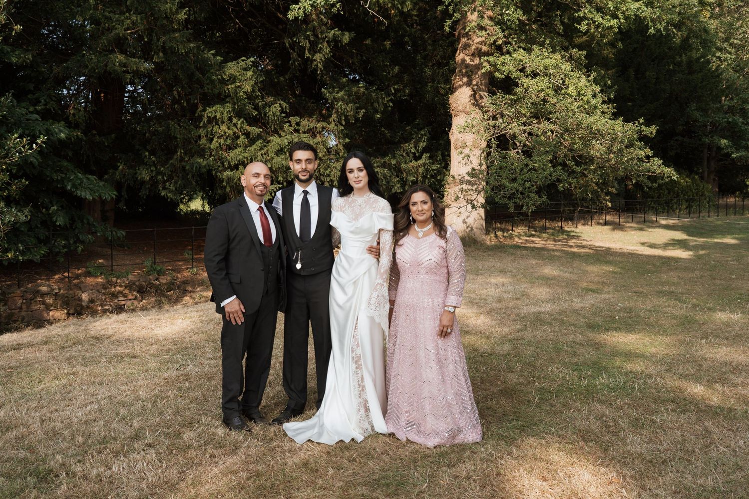 Wedding party poses for outdoor photos in a garden setting with trees and natural lighting.