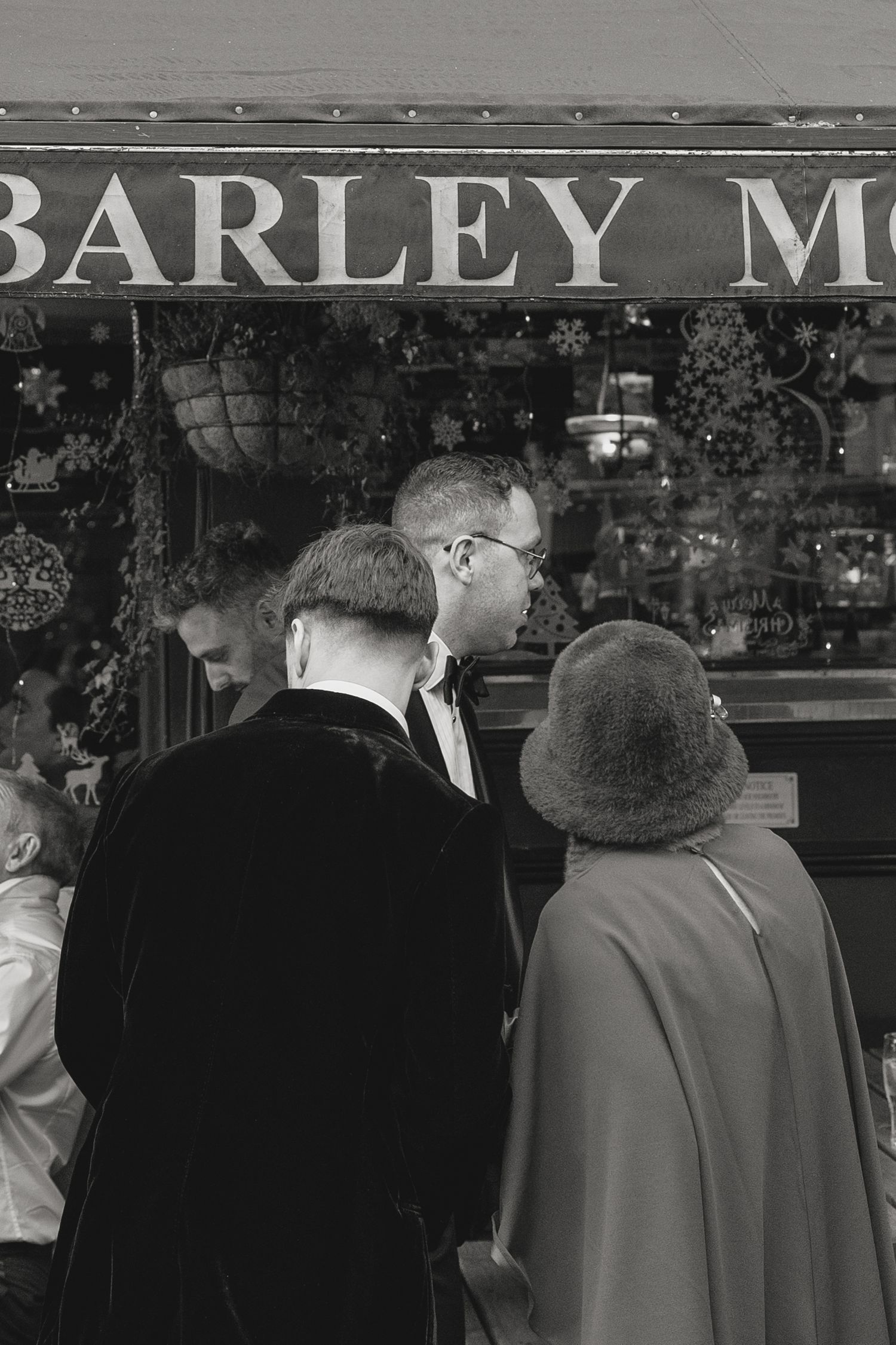 A group of people in formal attire stand outside a storefront with Barley M signage.