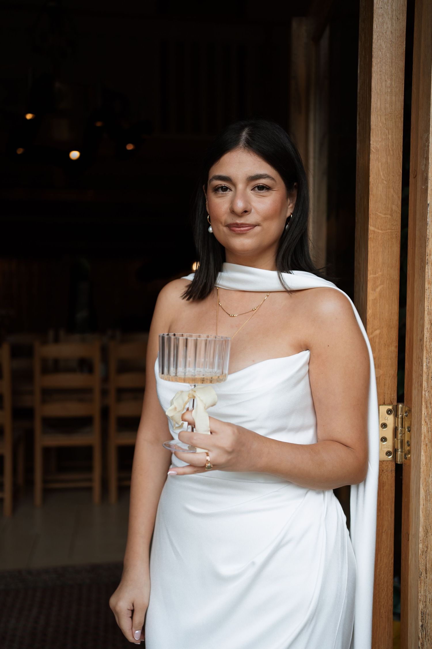 Figure in a white dress holding a glass in an elegant indoor setting.