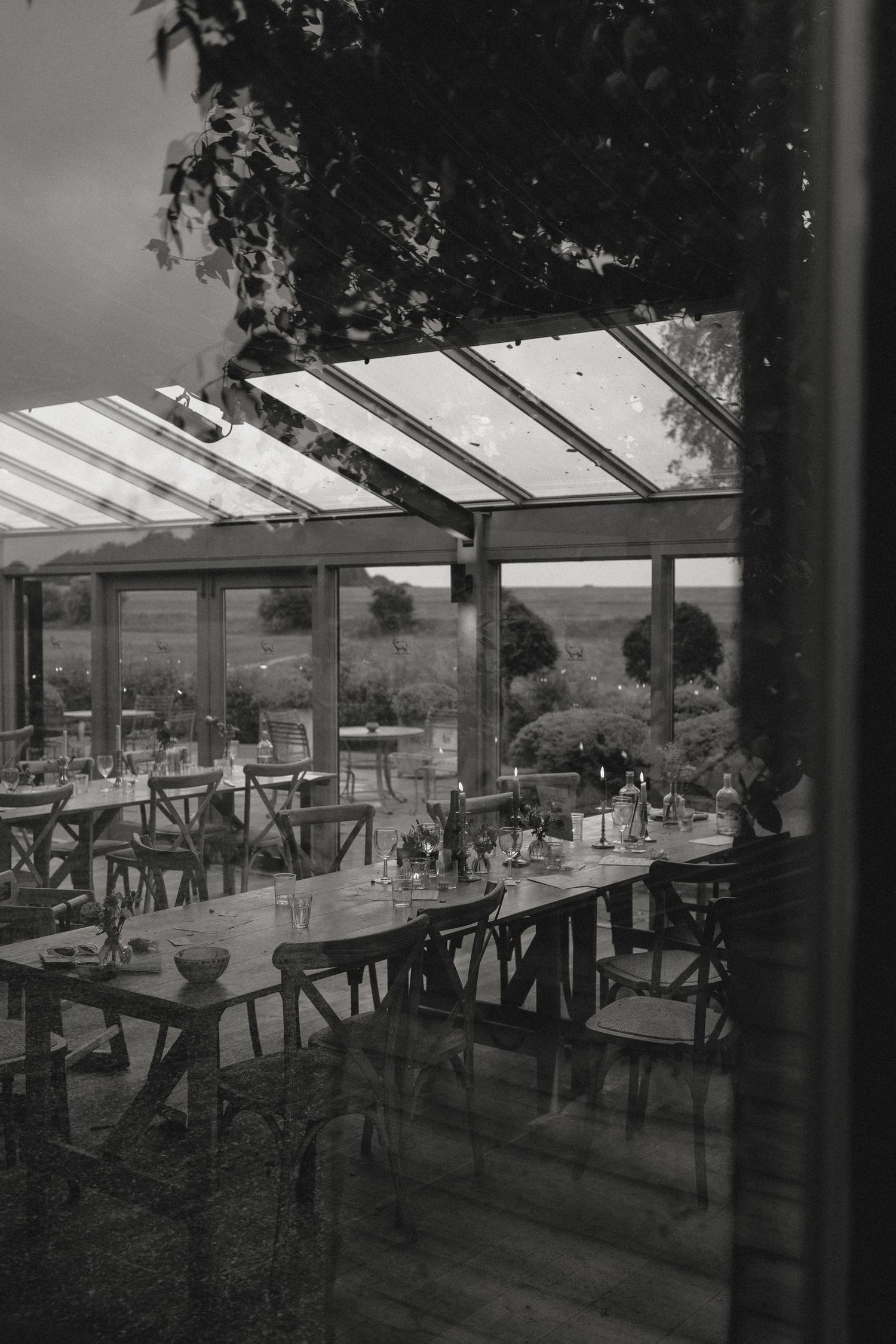 Modern outdoor dining area with glass roof and wooden tables arranged in rows.