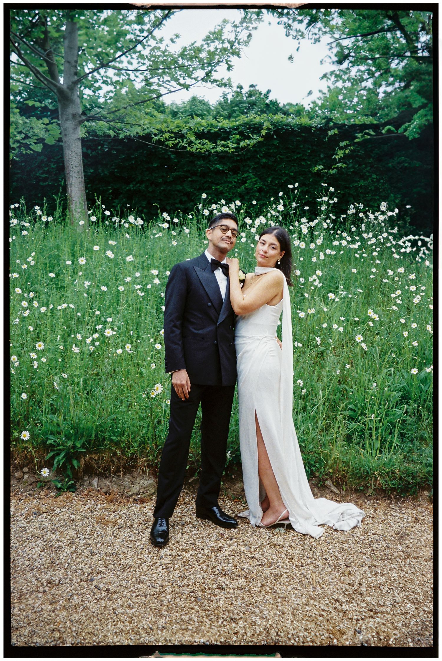 Couple in wedding attire posing in a field of white wildflowers.