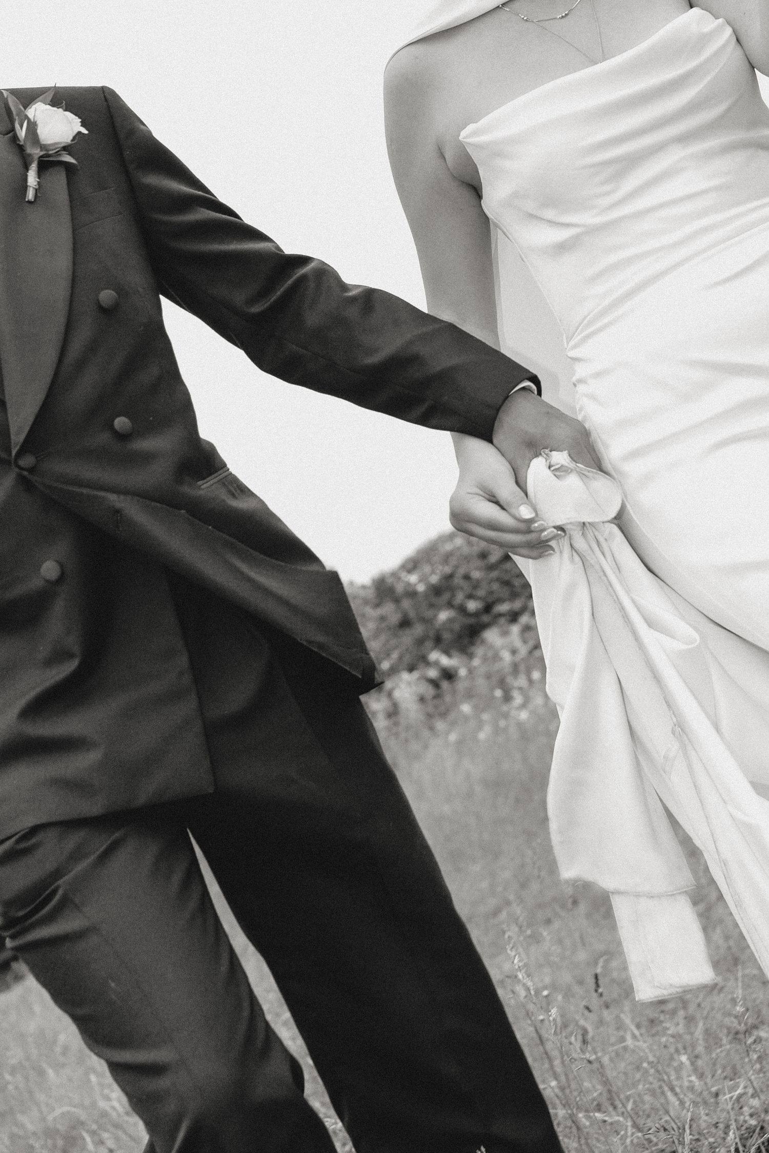 Black and white photo of bride and groom holding hands, walking outdoors on their wedding day.