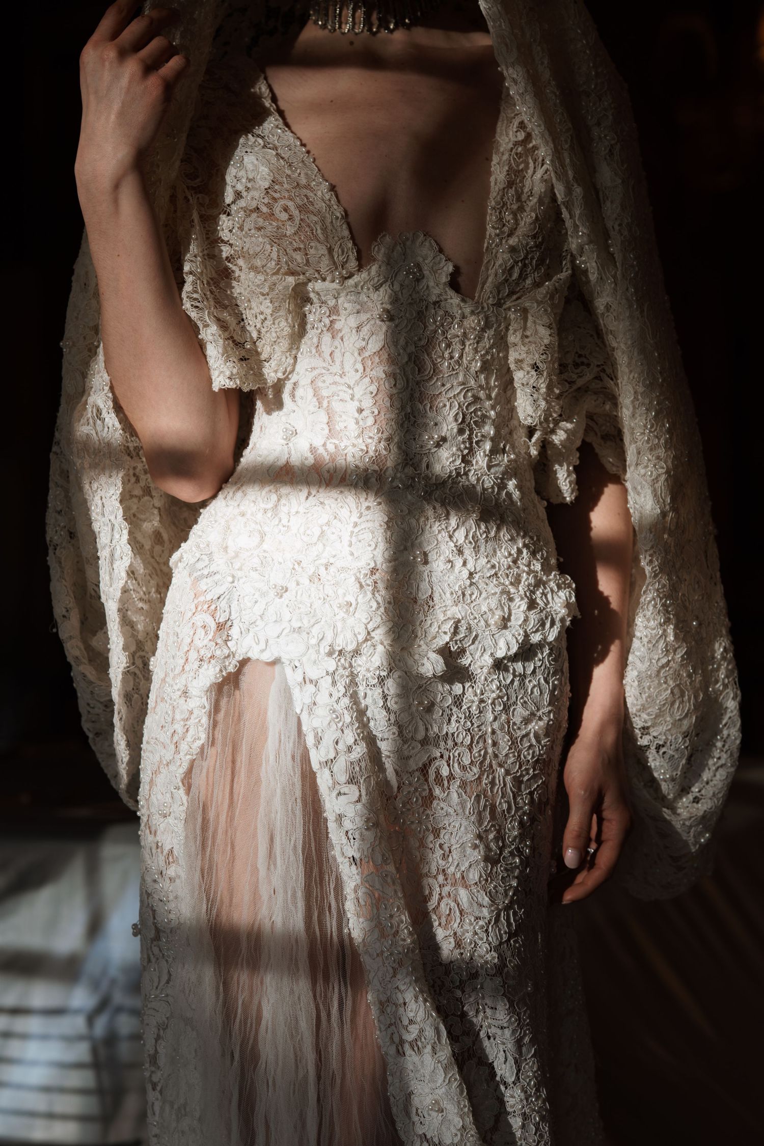 Elegant white lace wedding dress with deep V-neckline and sheer skirt, draped in soft natural light.