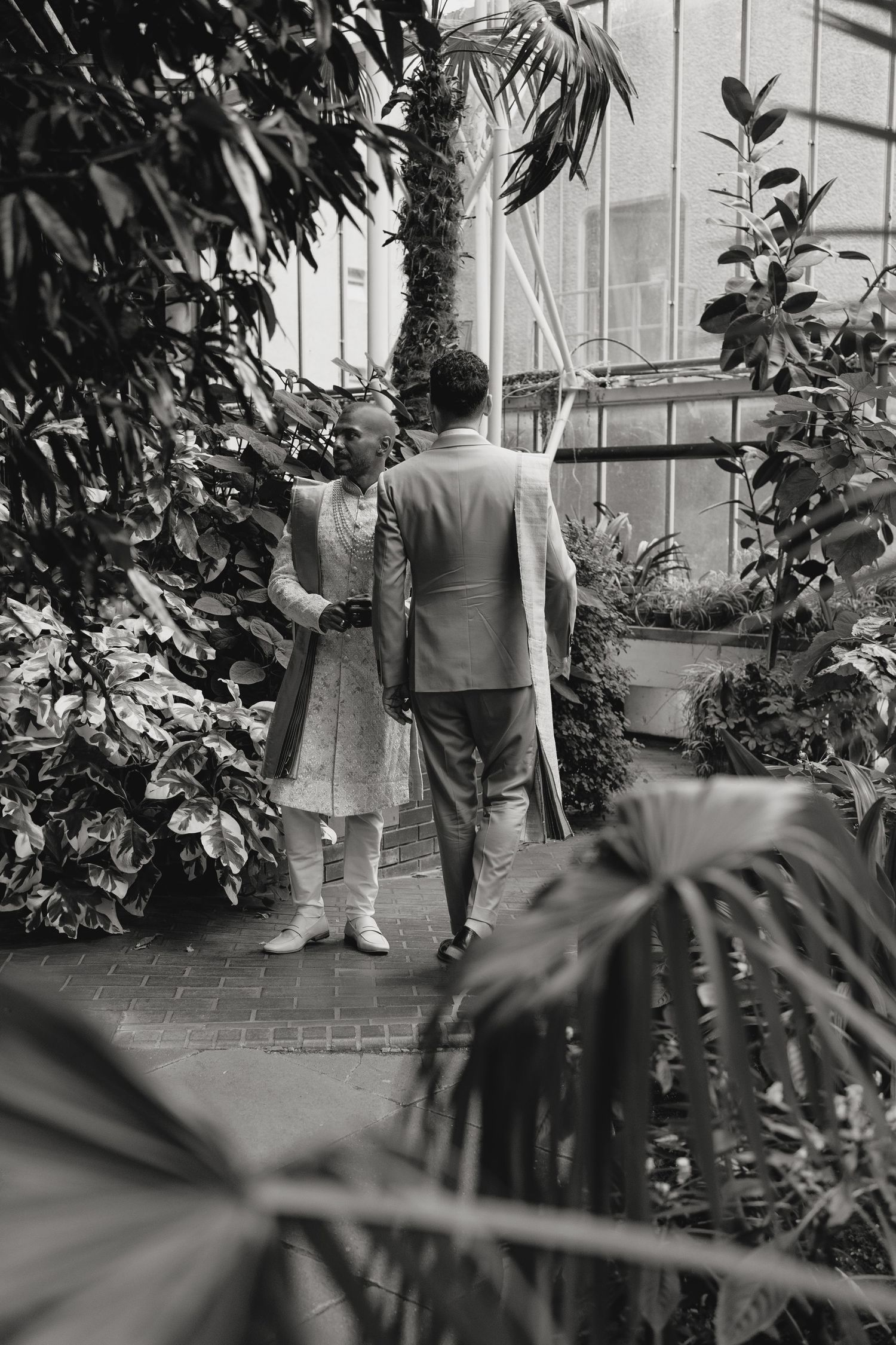 Black and white photo of people walking through a greenhouse with lush plants.