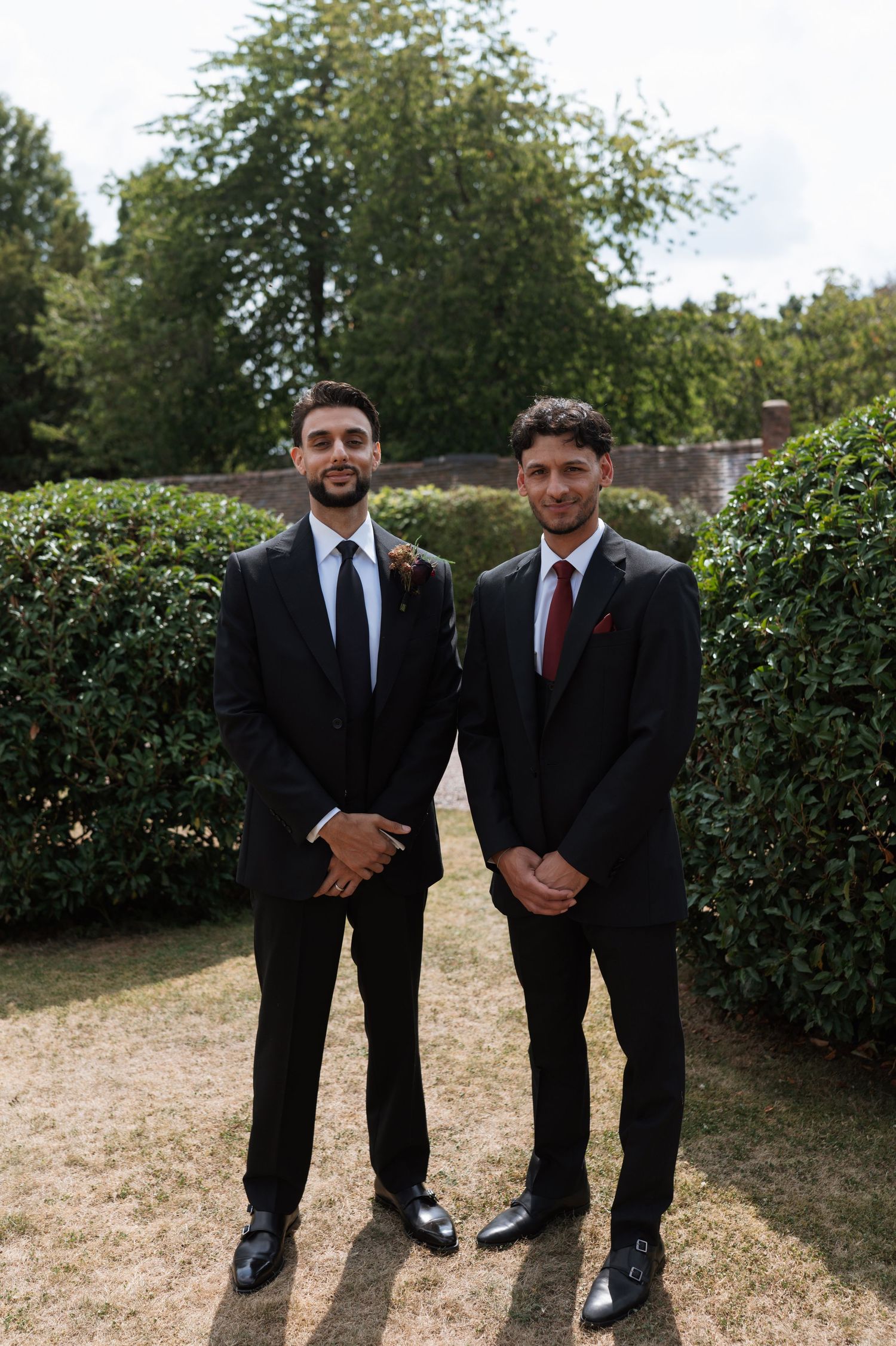 Two people in dark suits standing in a garden setting.