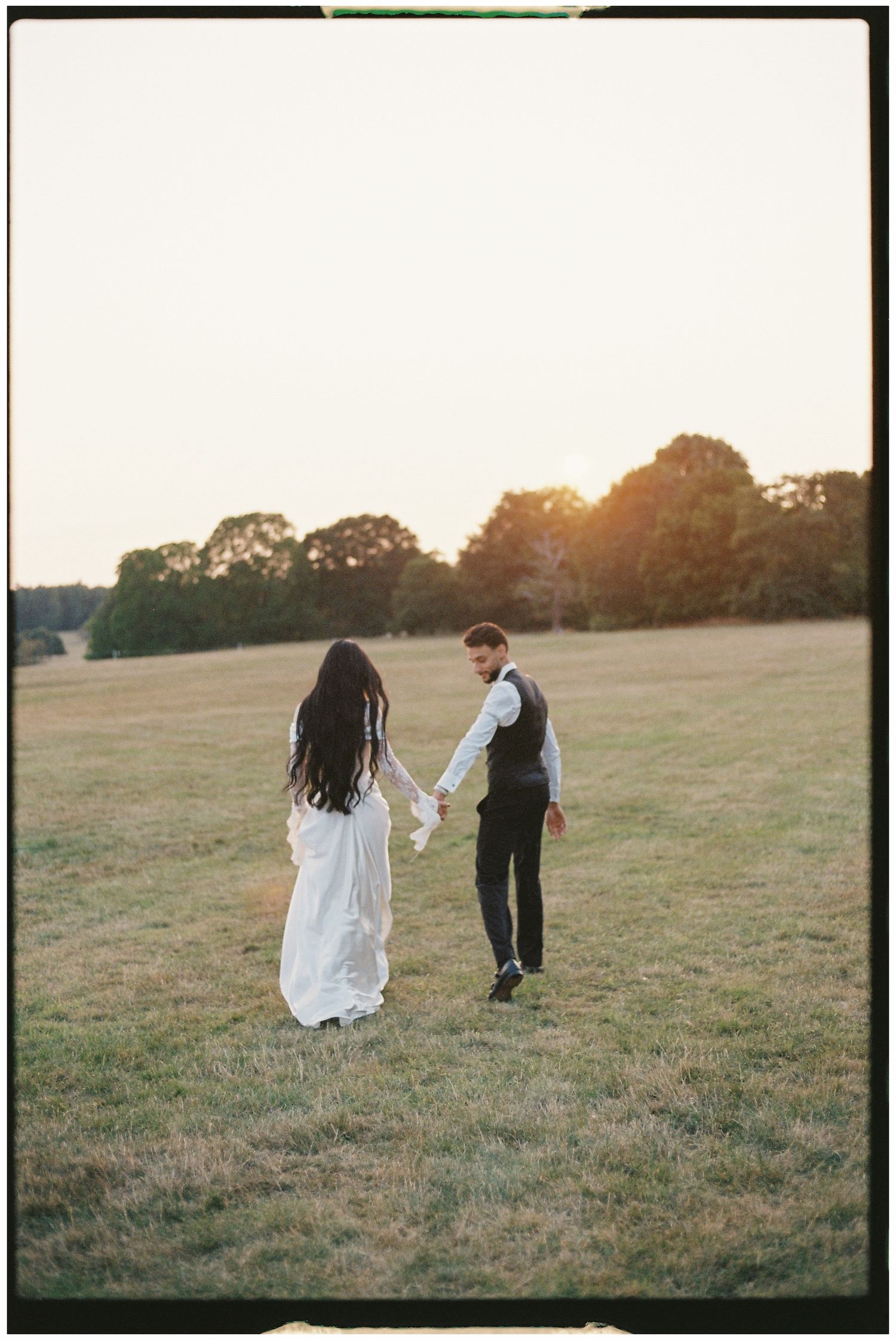 Couple holding hands while walking in a sunset field.