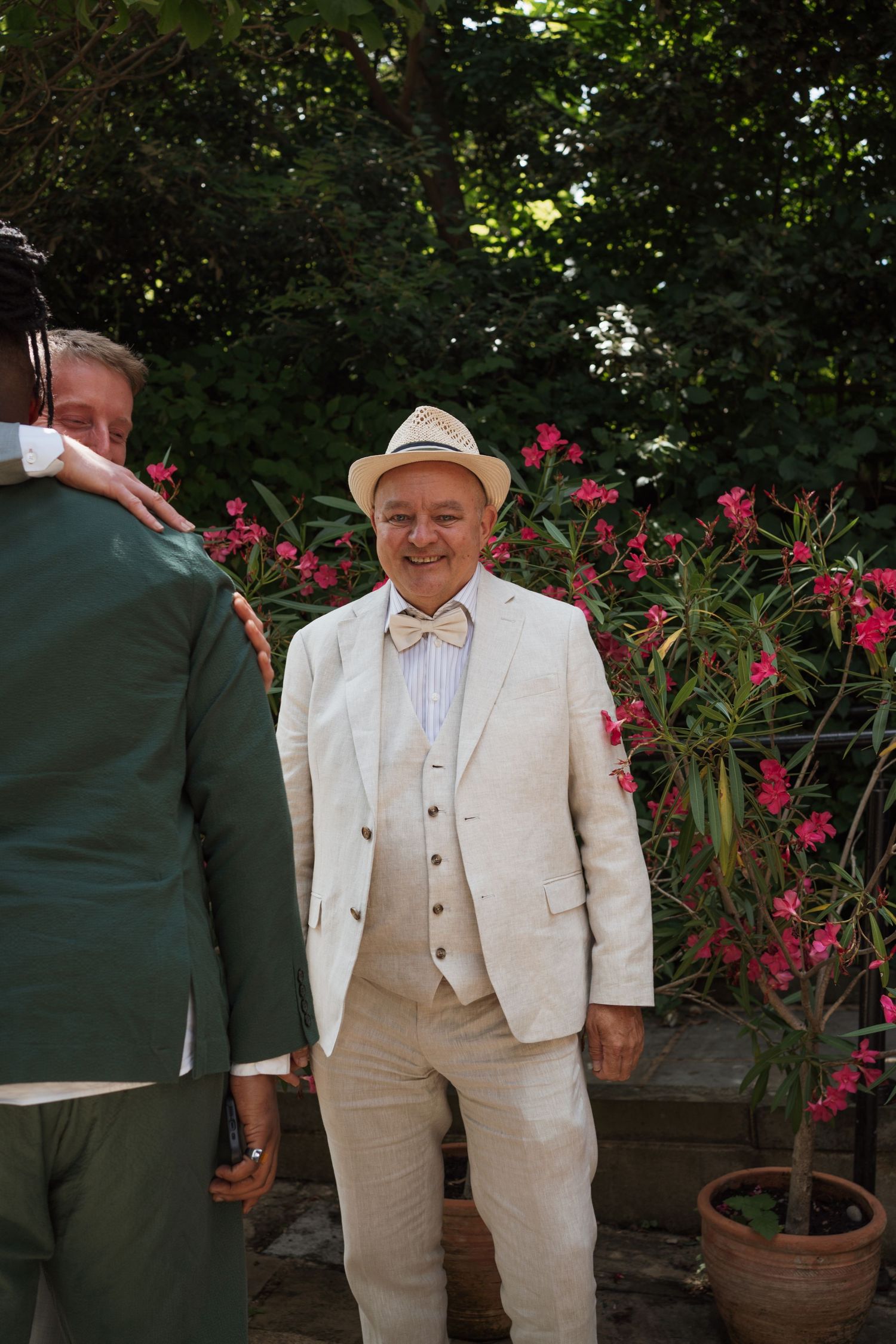 Guests in light and dark colored suits chatting near potted flowers in a garden.