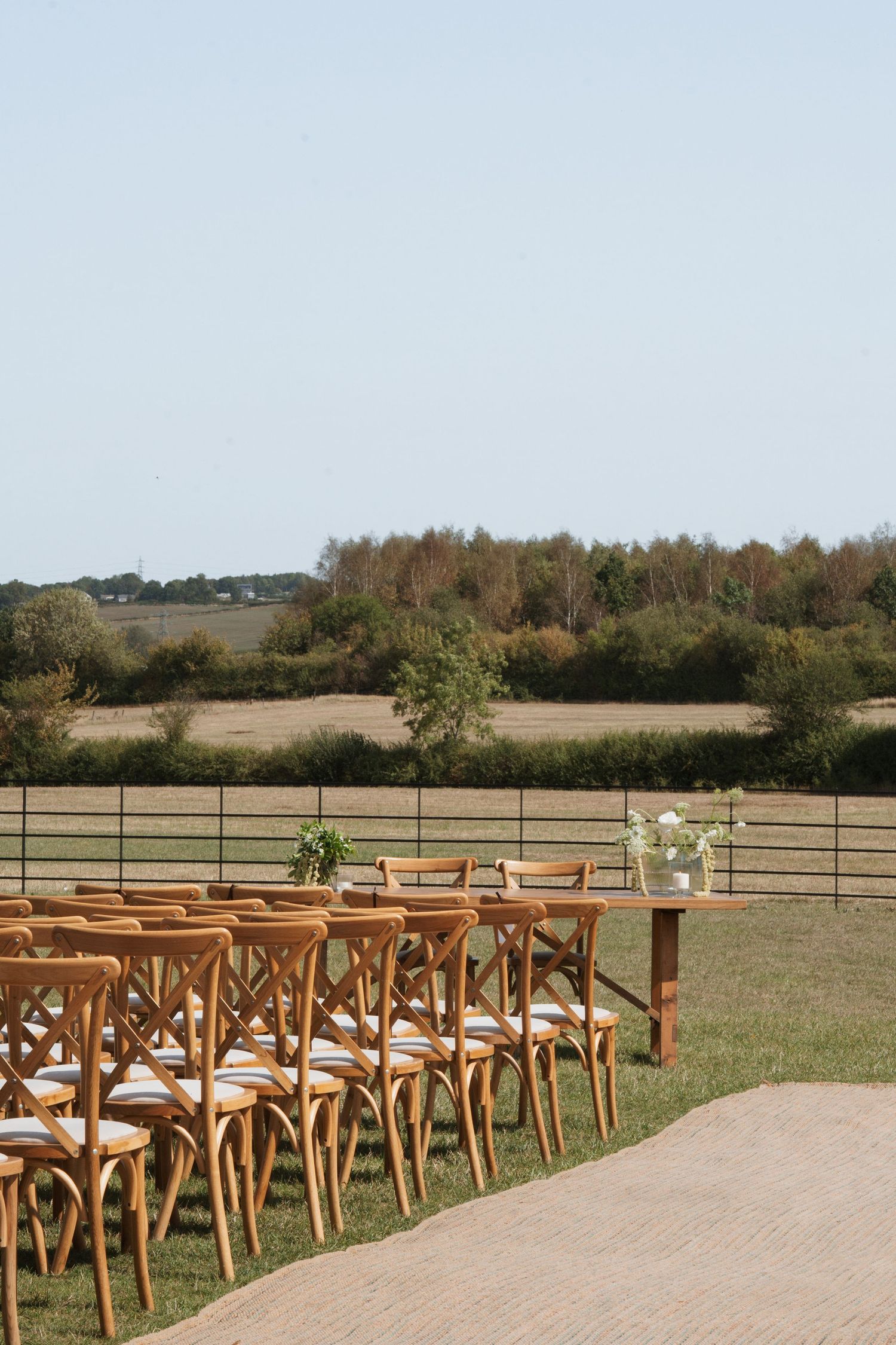 Outdoor wedding setup with wooden cross-back chairs facing a natural landscape.