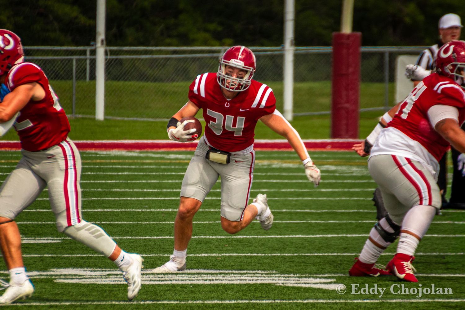 Football player in red uniform carries ball between defenders on field.