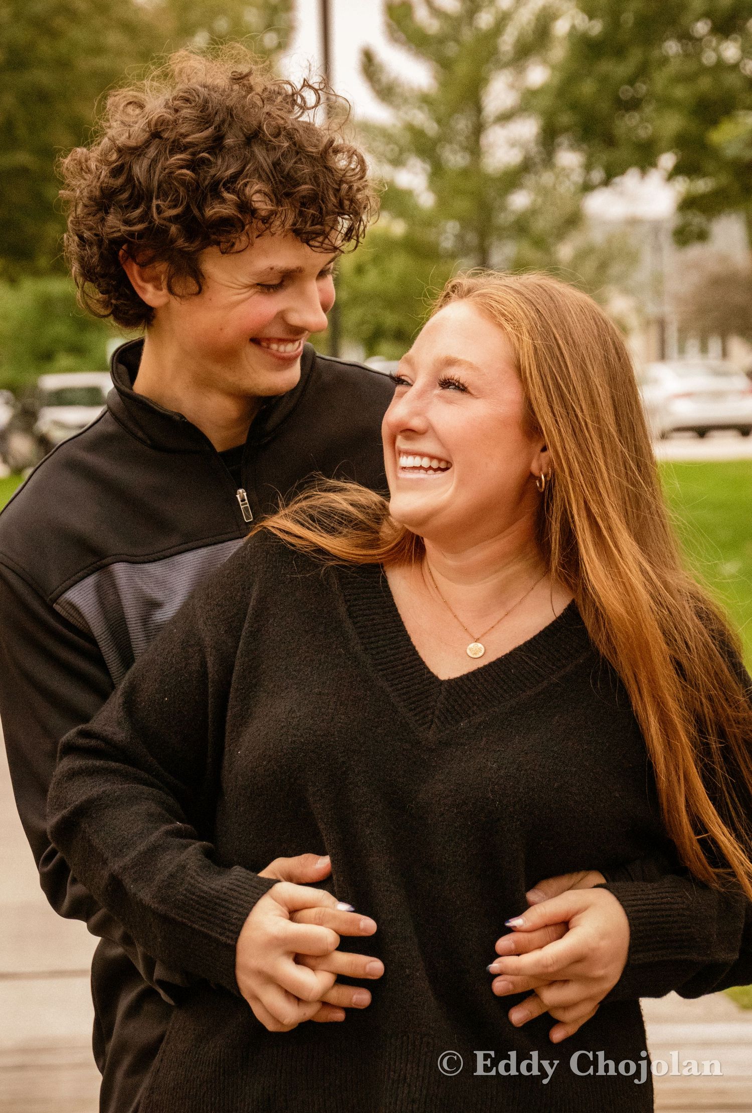 A couple in matching black sweaters share a joyful moment outdoors.