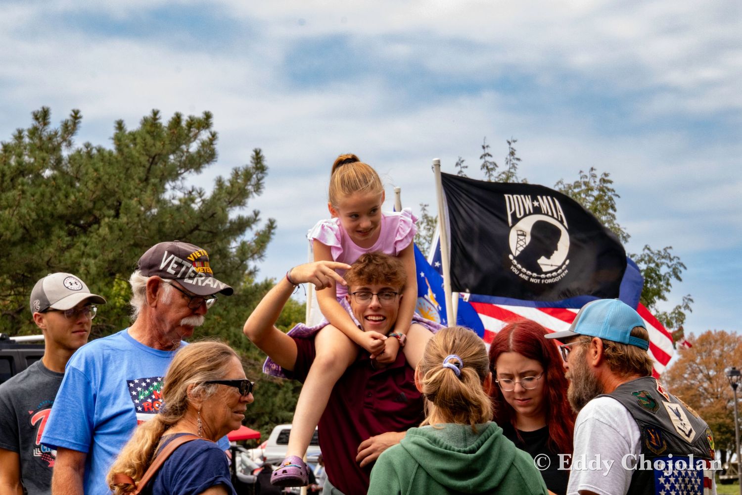 Crowd watching event with POW MIA flag and balloons visible.