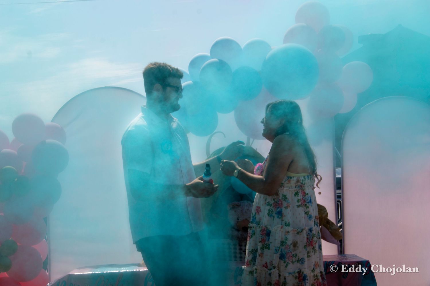 Colorful smoke and balloon decorations create a dreamy atmosphere at an outdoor gender reveal party.