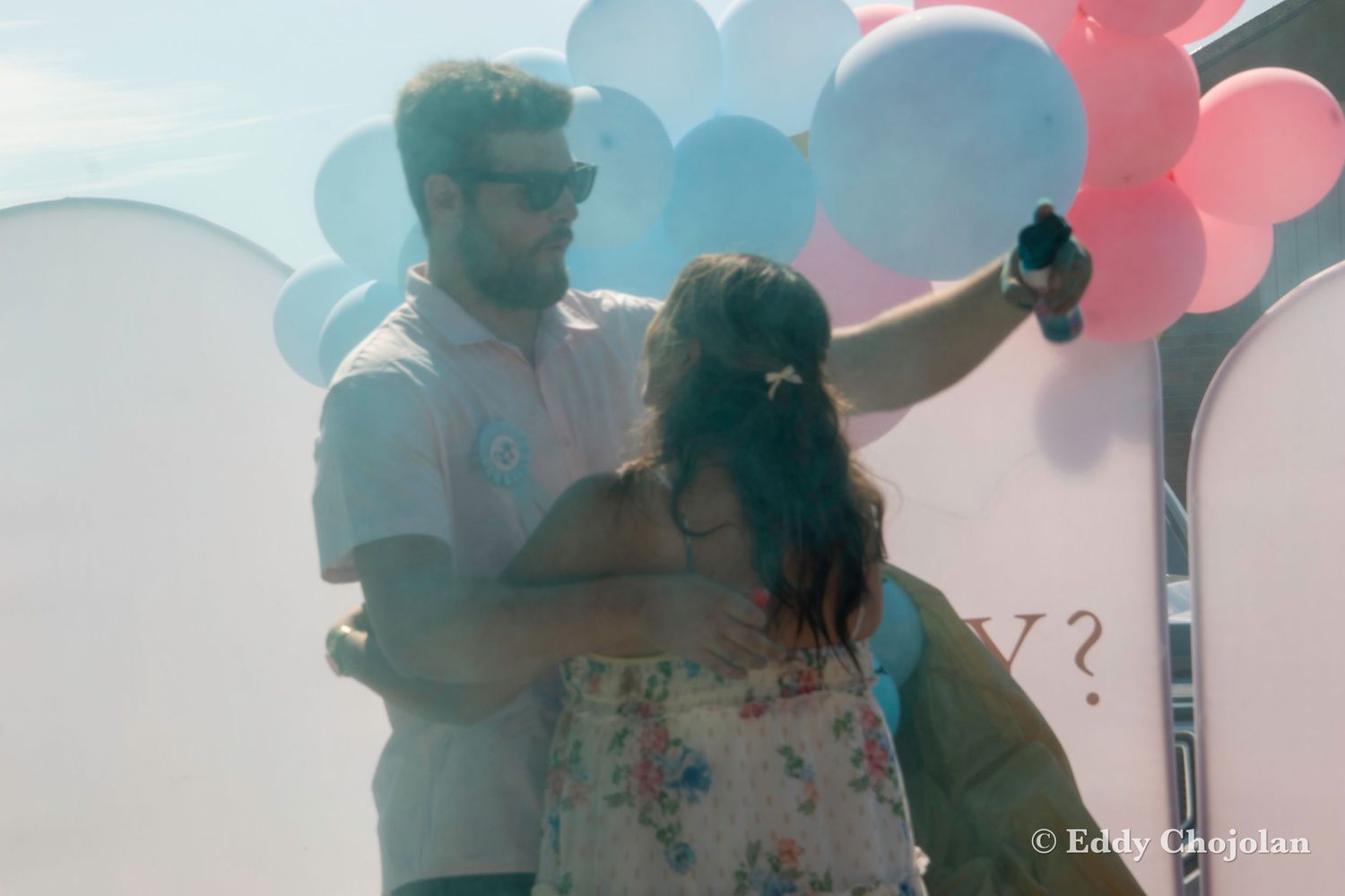Couple poses in front of decorative balloon arch at outdoor event.