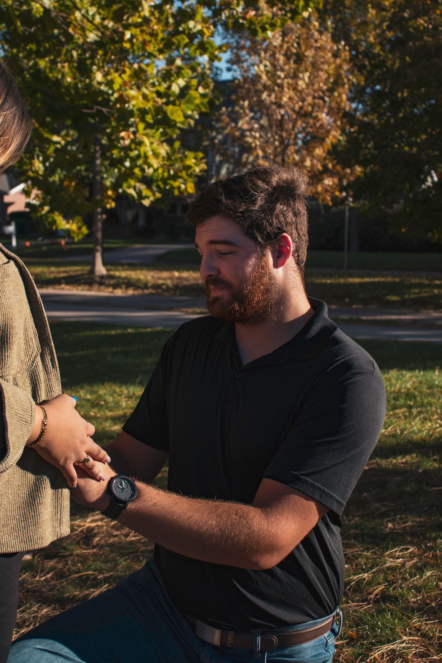 Person in black shirt sitting outdoors against a backdrop of fall trees.