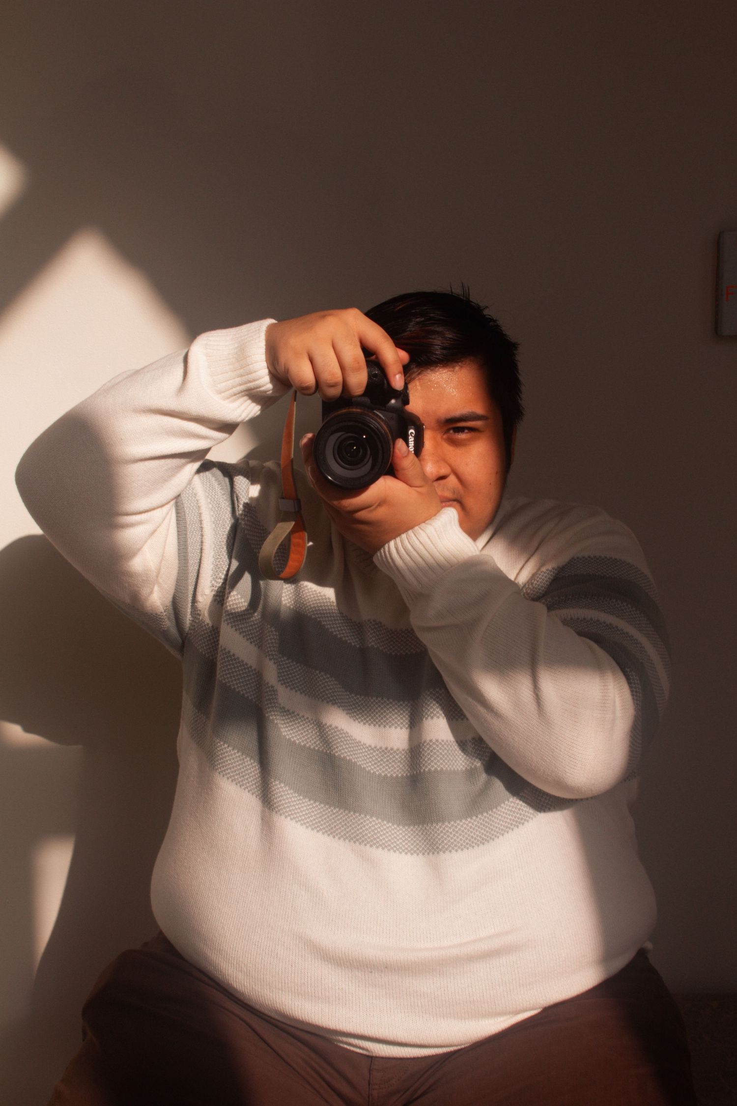 A photographer in a white sweater takes photos with a DSLR camera against a dark background in a series of shots.