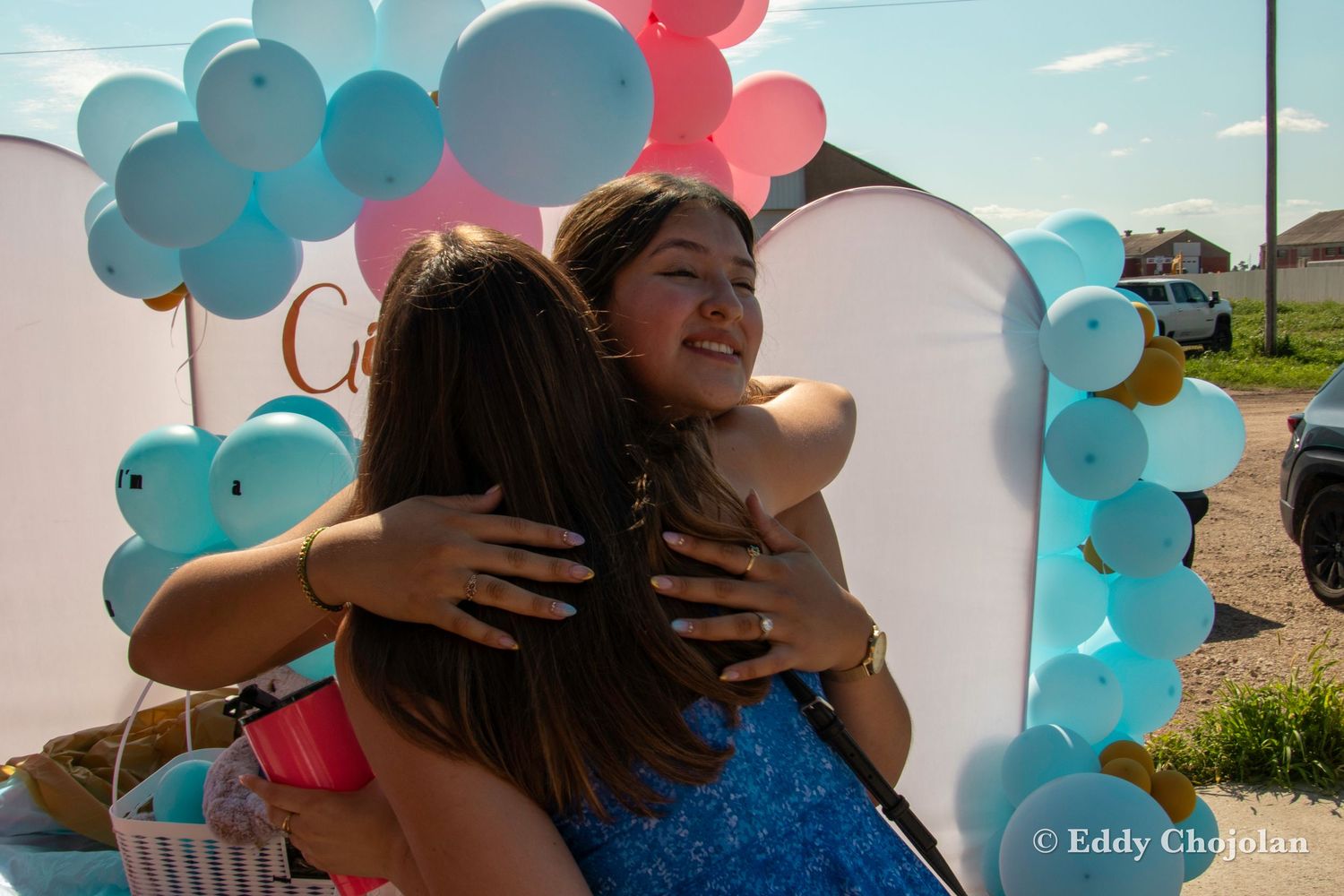 Emotional embrace at a gender reveal party decorated with pink and blue balloons.
