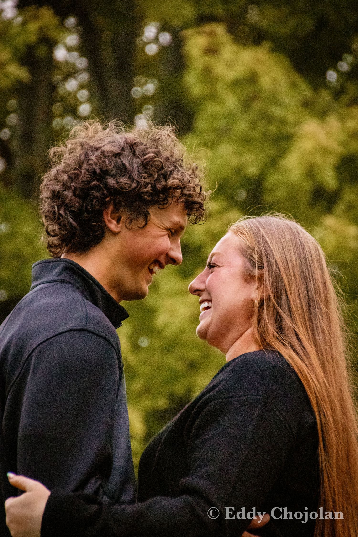A couple shares a laughing moment together outdoors in black sweaters.