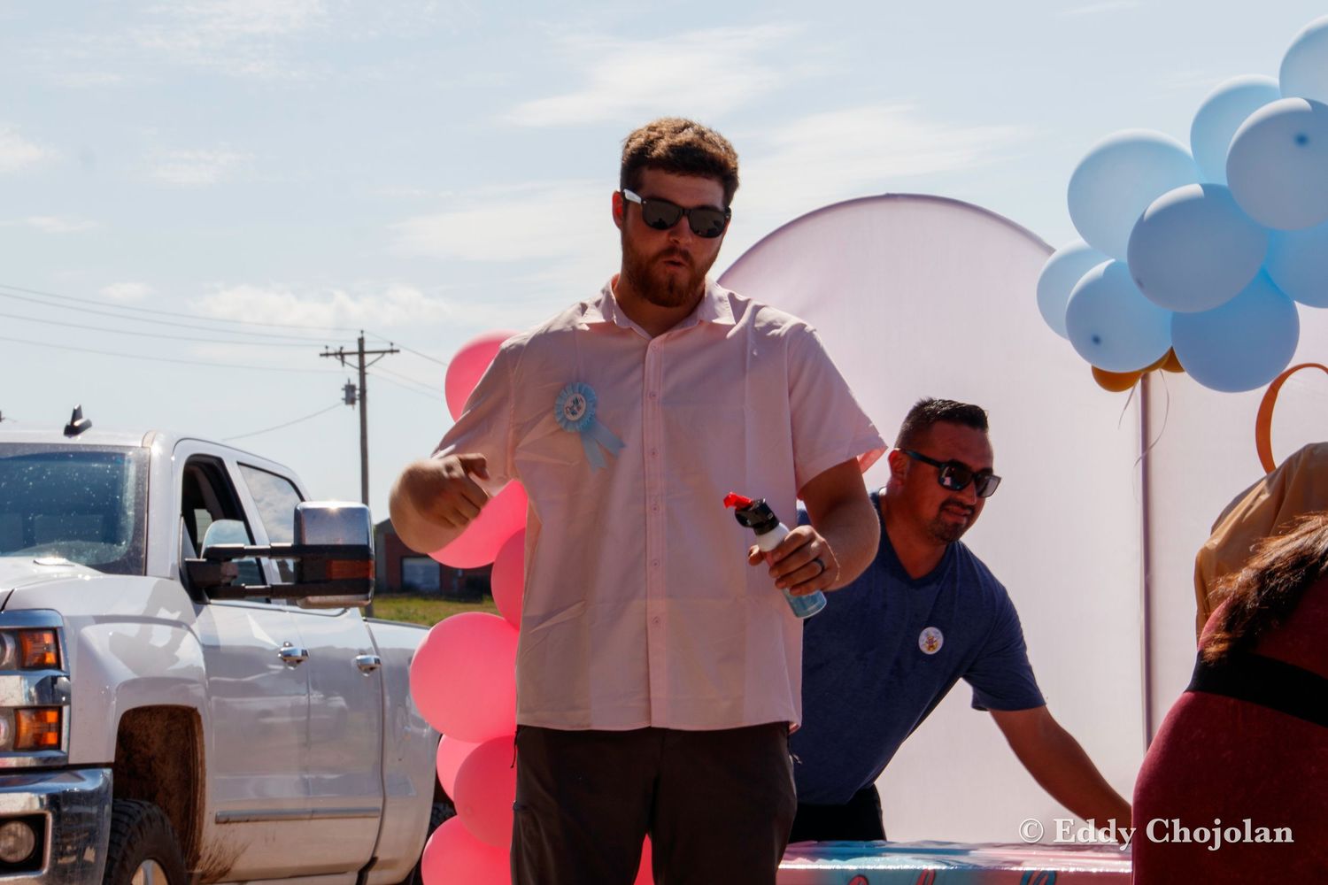 Outdoor gender reveal party setup with blue and pink balloon arch decorations on a sunny day.