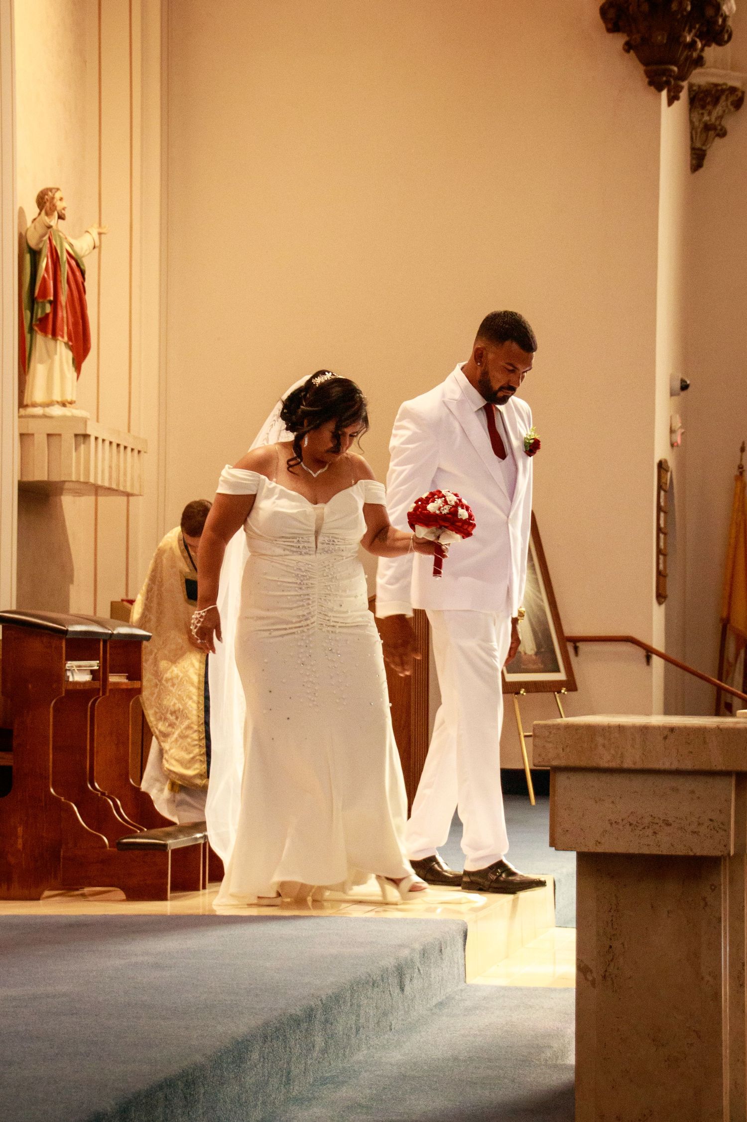 Wedding ceremony in a church with people in white formal attire standing at the altar steps.