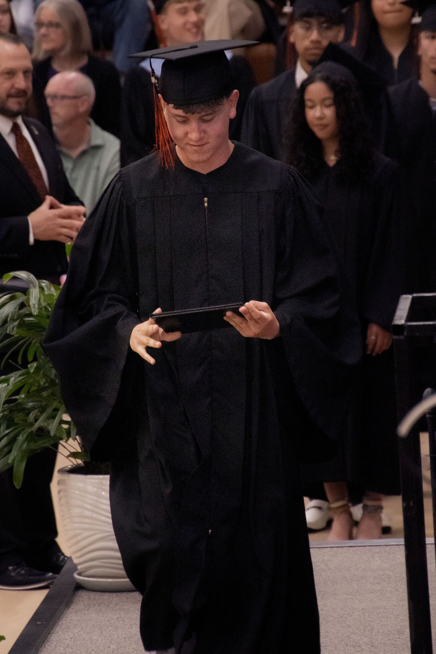 Graduate in traditional black academic regalia reads from diploma holder.