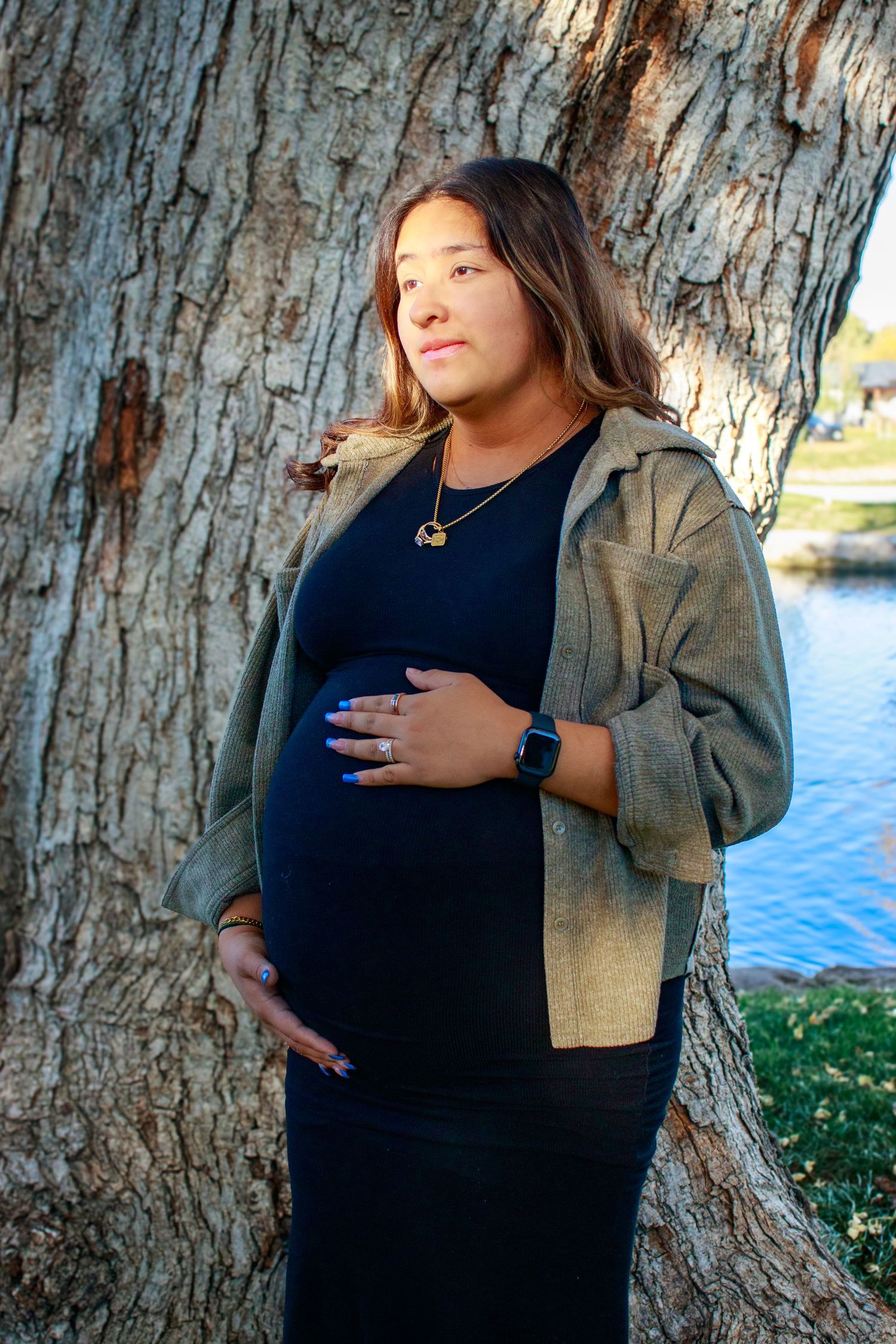 Maternity photoshoot by a large tree trunk near water.