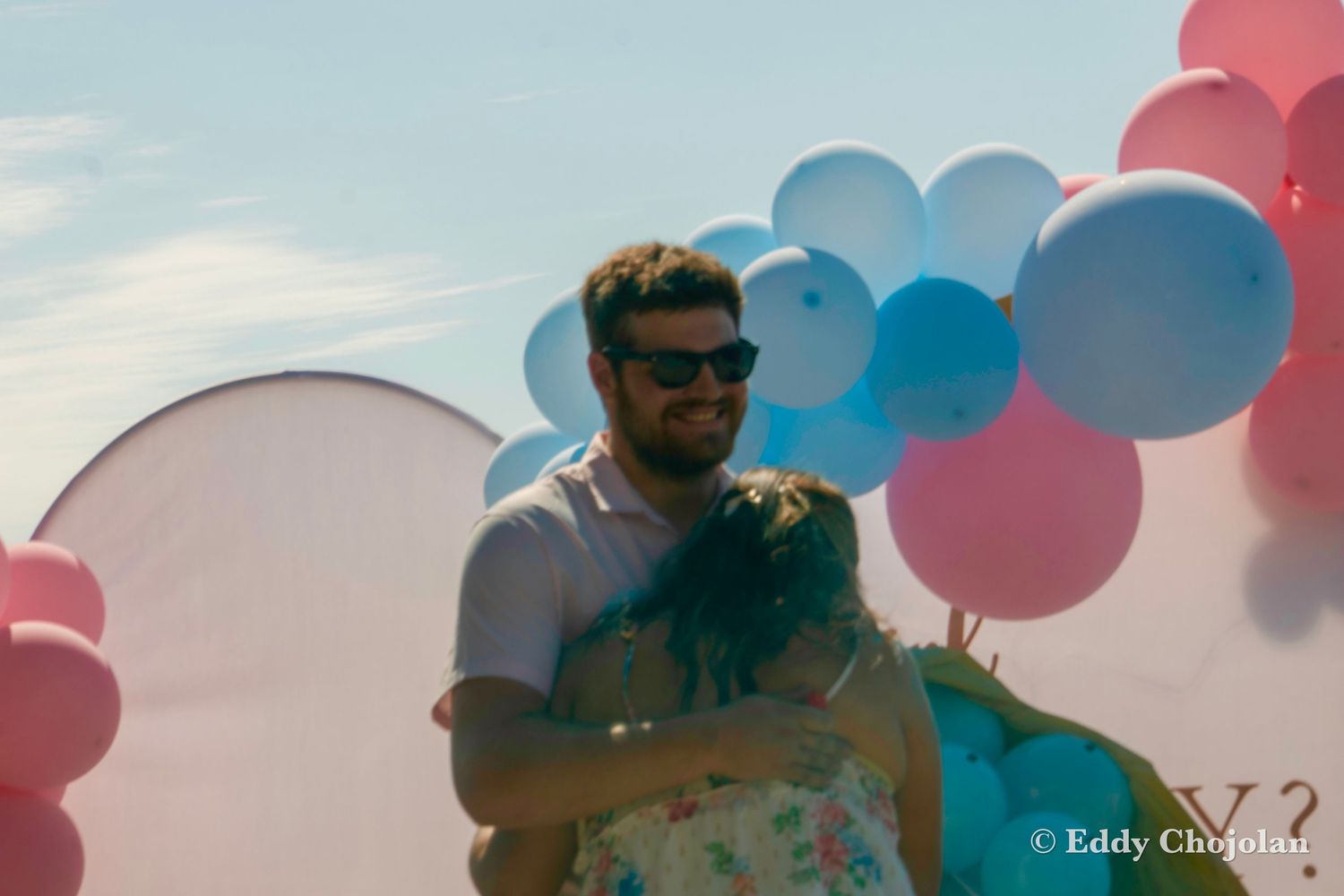 Outdoor celebration setup with pink and blue balloon arch decoration.